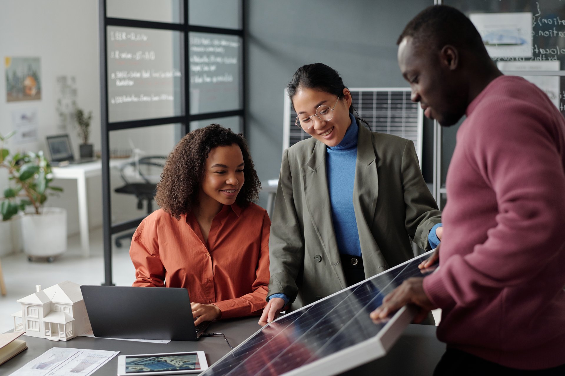 Young African American businesswoman looking at model of solar panel while her colleagues presenting their project at working meeting