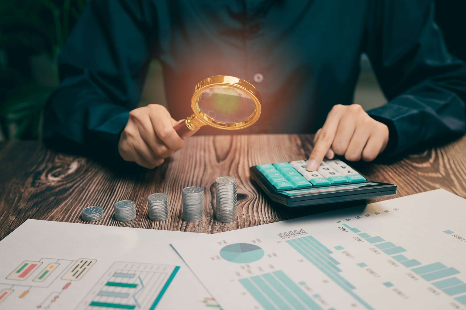 A Detailed Financial Analysis with Calculator, Coins, and Magnifying Glass on a Wooden Table, Business concept