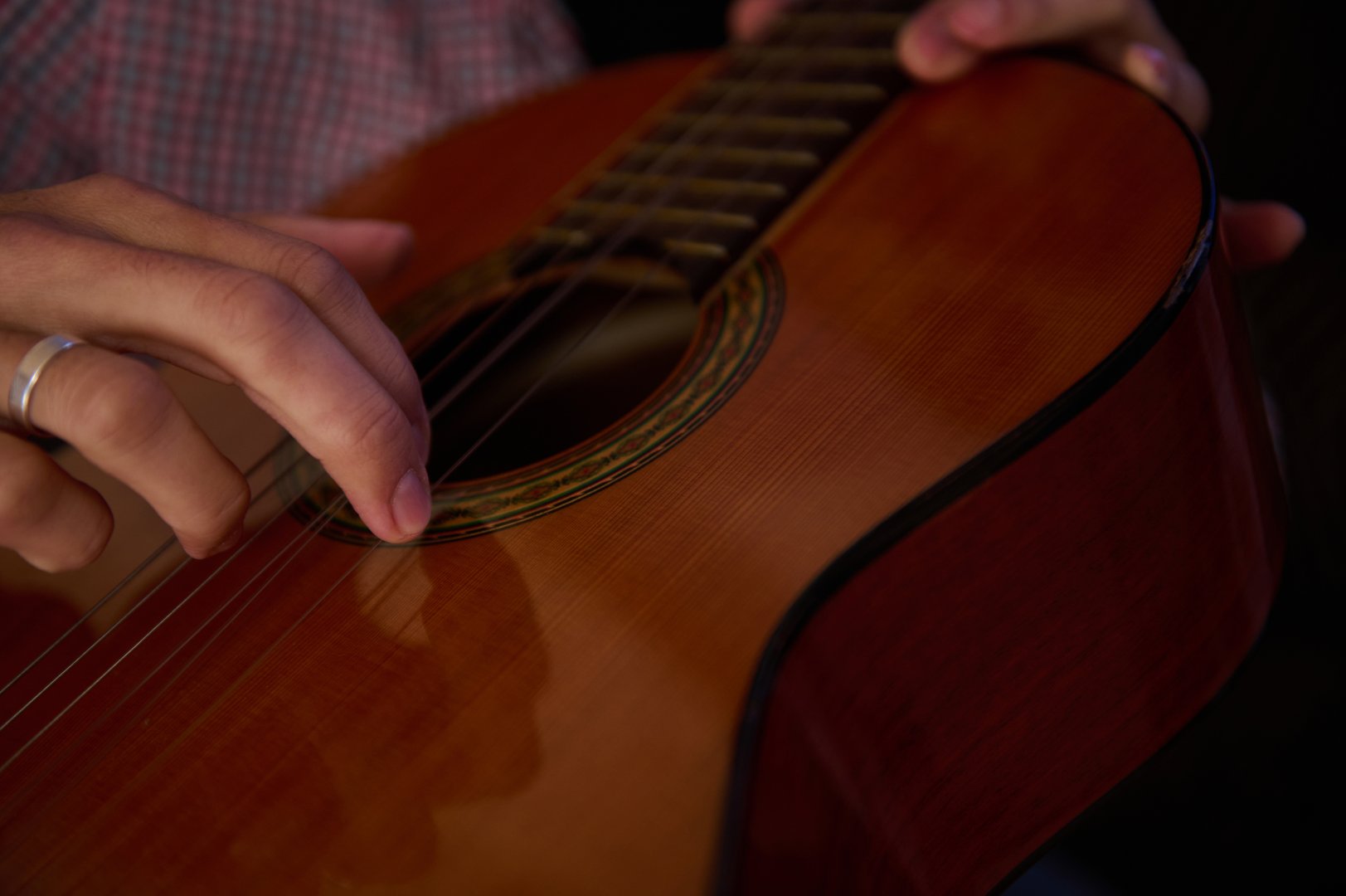 Close-up image of a person strumming a classical guitar, focusing on precise hand movements, evoking a sense of musical skill and passion for playing stringed instruments.
