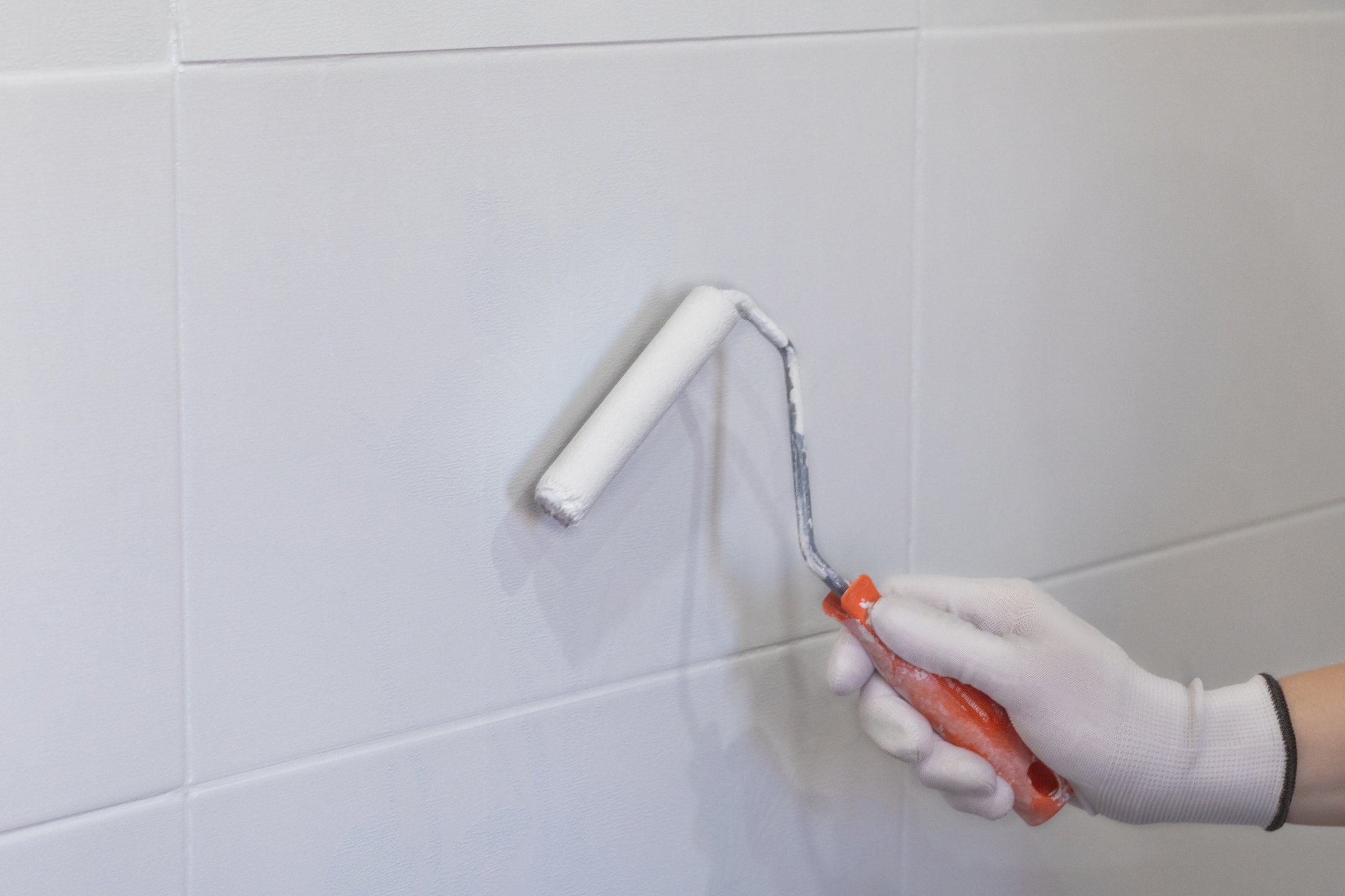 Painting tiles in the kitchen in the bathroom, white paint with a roller. Hand in glove with roller close up photo