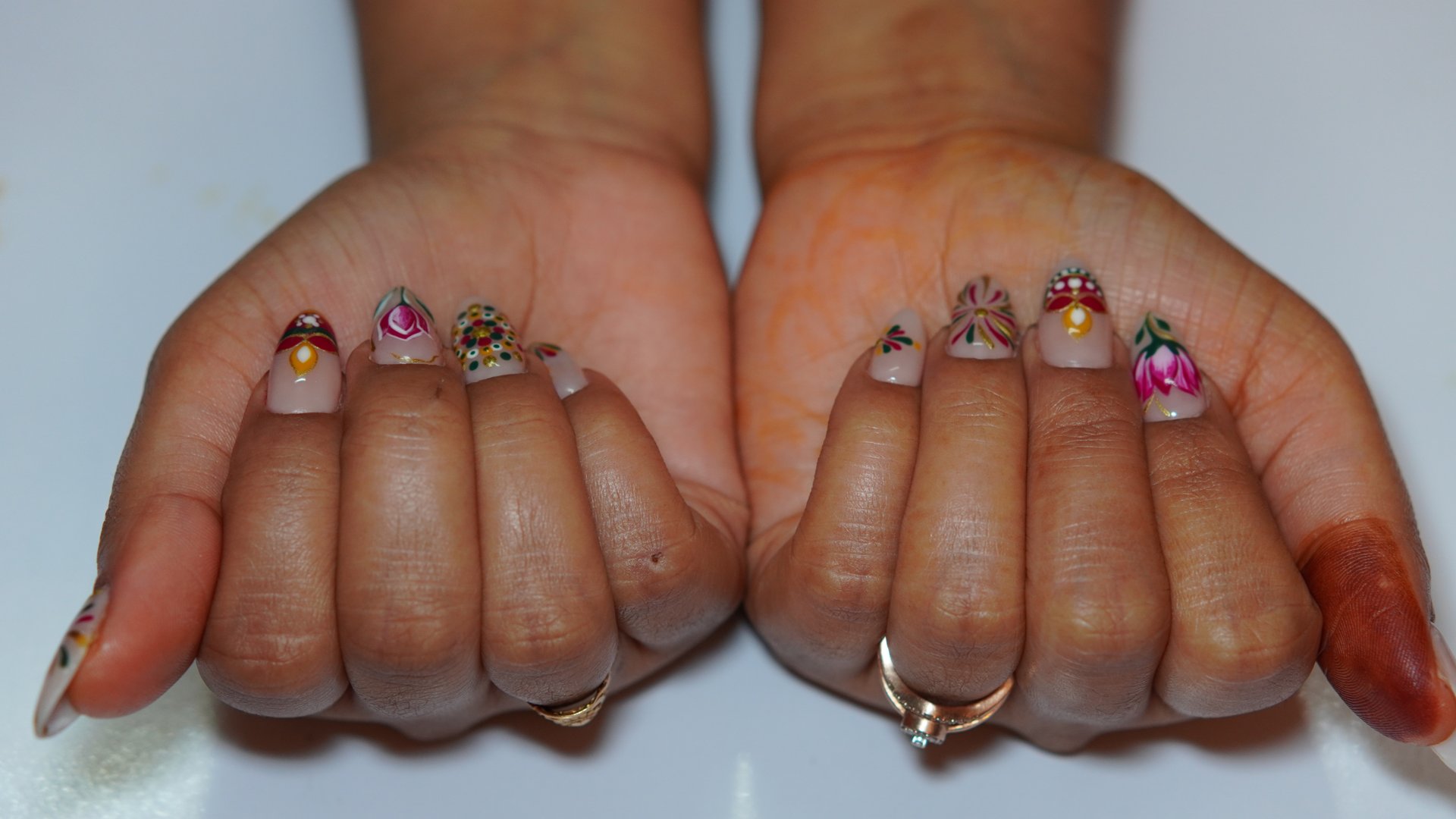Close-up of a woman's hand featuring intricate Diwali-themed nail art. The design incorporates traditional Indian patterns, vibrant colors like red, gold, and orange, and decorative elements such as diyas (lamps), rangoli, and glitter. The background is festive, highlighting the celebratory mood of Diwali. Perfect for use in beauty, culture, and holiday-related content.