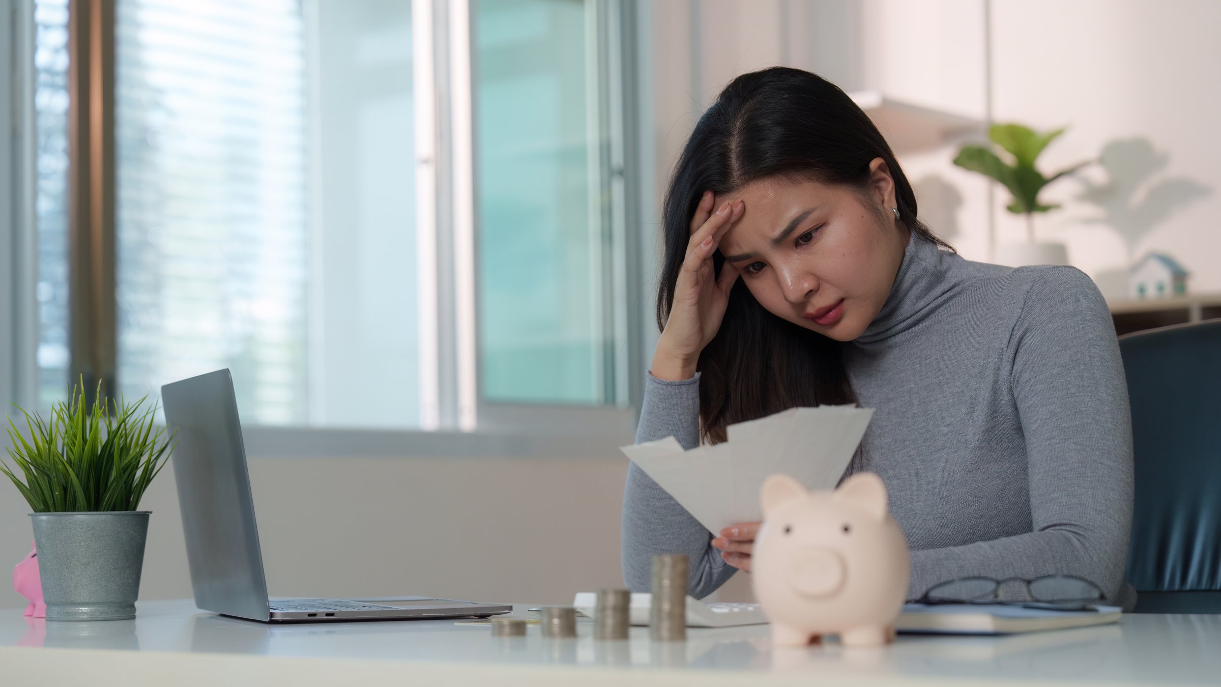 A young woman feels overwhelmed while analyzing her finances and bills at a home office, reflecting financial stress and budgeting challenges.