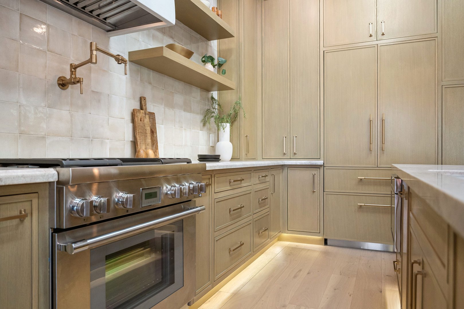 Modern kitchen with stainless steel appliances, wooden cabinets, and decorative shelves, featuring a minimalist design and soft lighting.