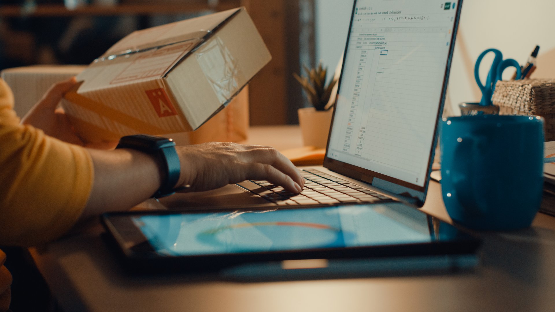 Young freelance Asian woman using laptop packing cardboard box in living room at home at night. Working from home.