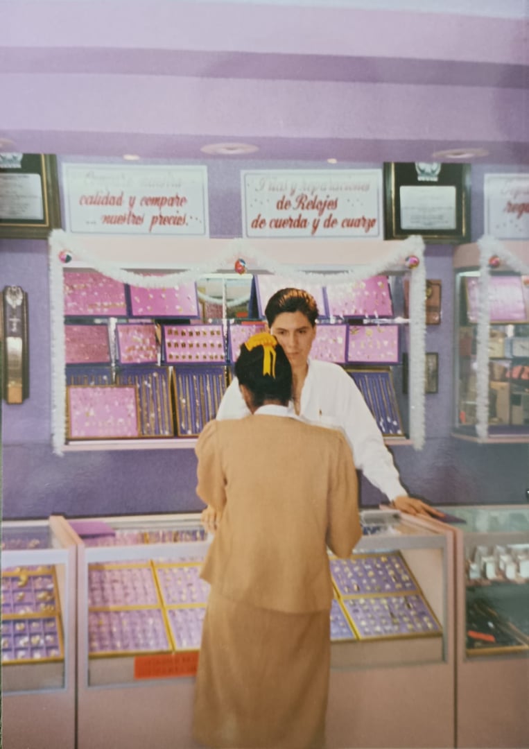 A customer at a jewelry store counter with staff, surrounded by display cases filled with various jewelry items.