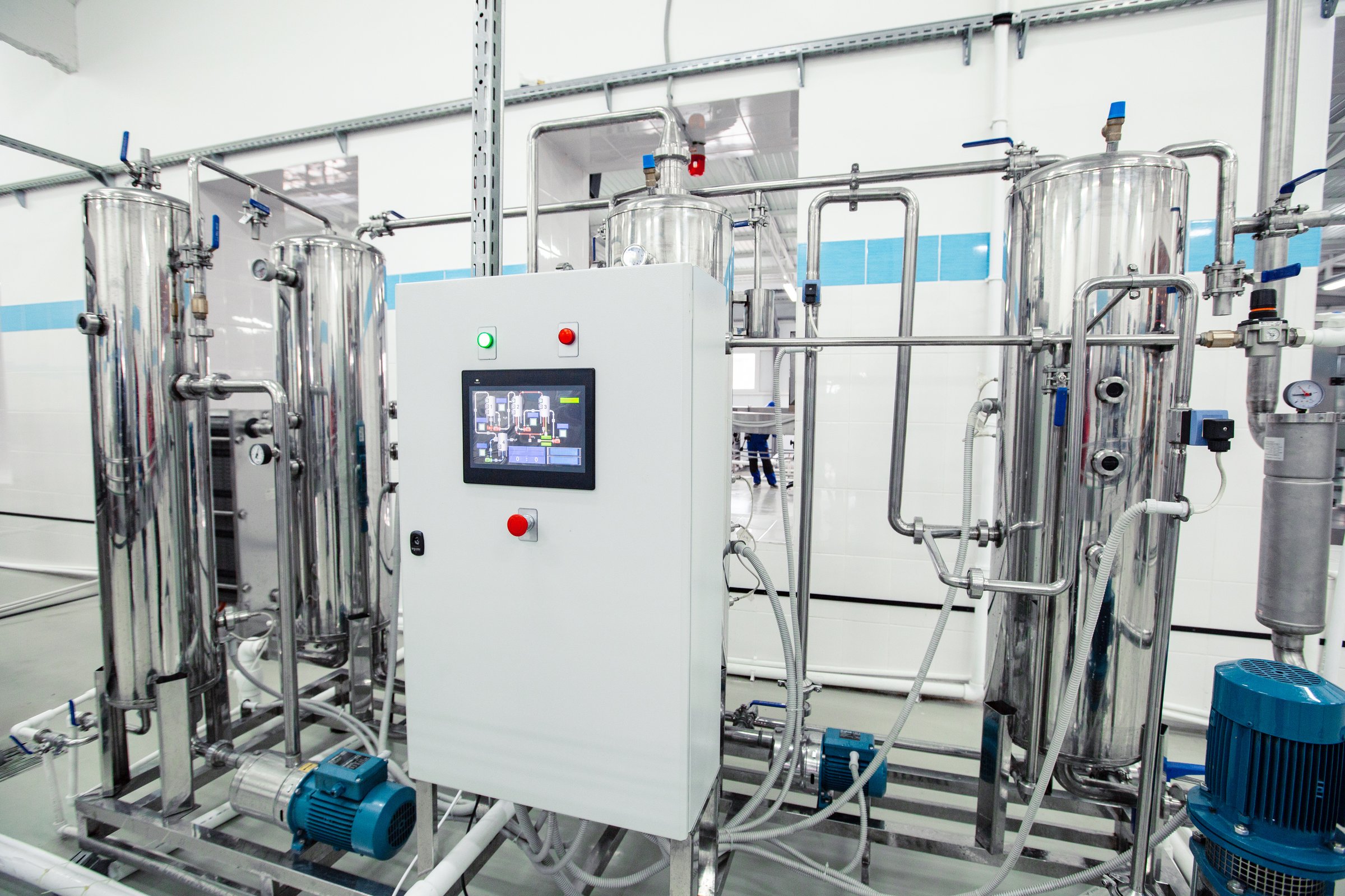 Large stainless steel processing equipment is displayed in a pristine factory. Featuring control panels and pipes, this setup focuses on efficiency and precision in production.