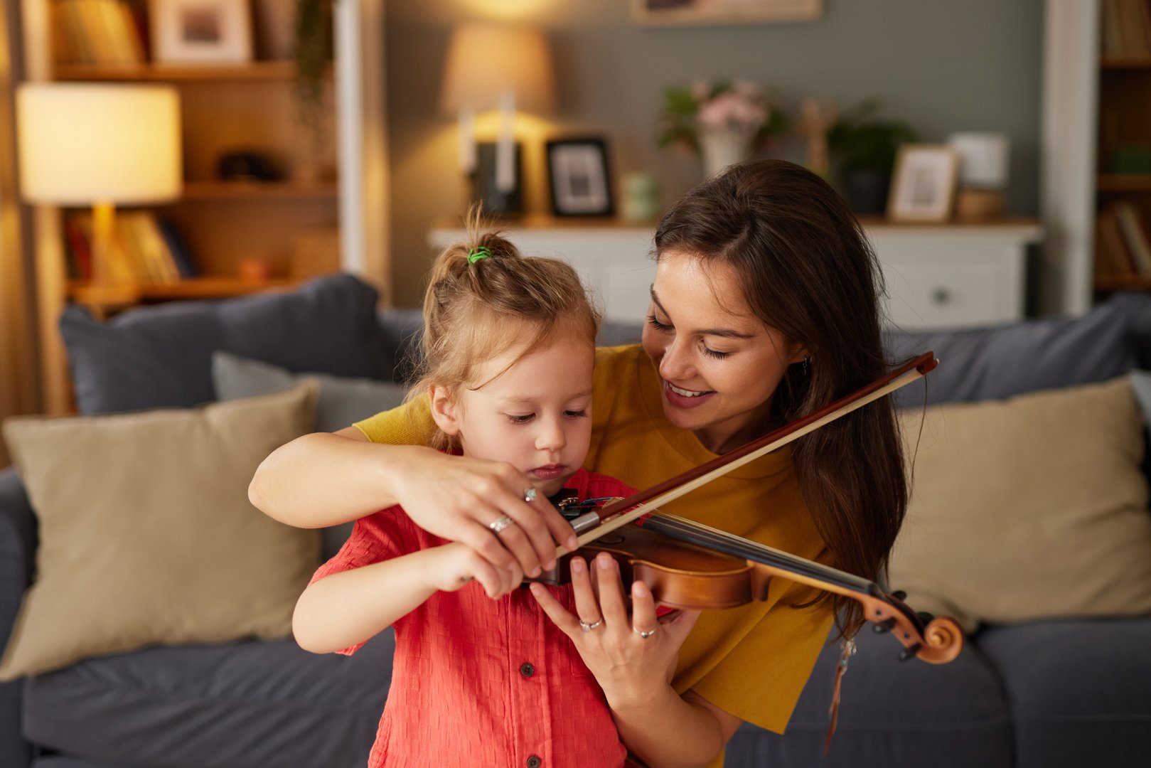 Mother and daughter learning to play the violin together in a living room
