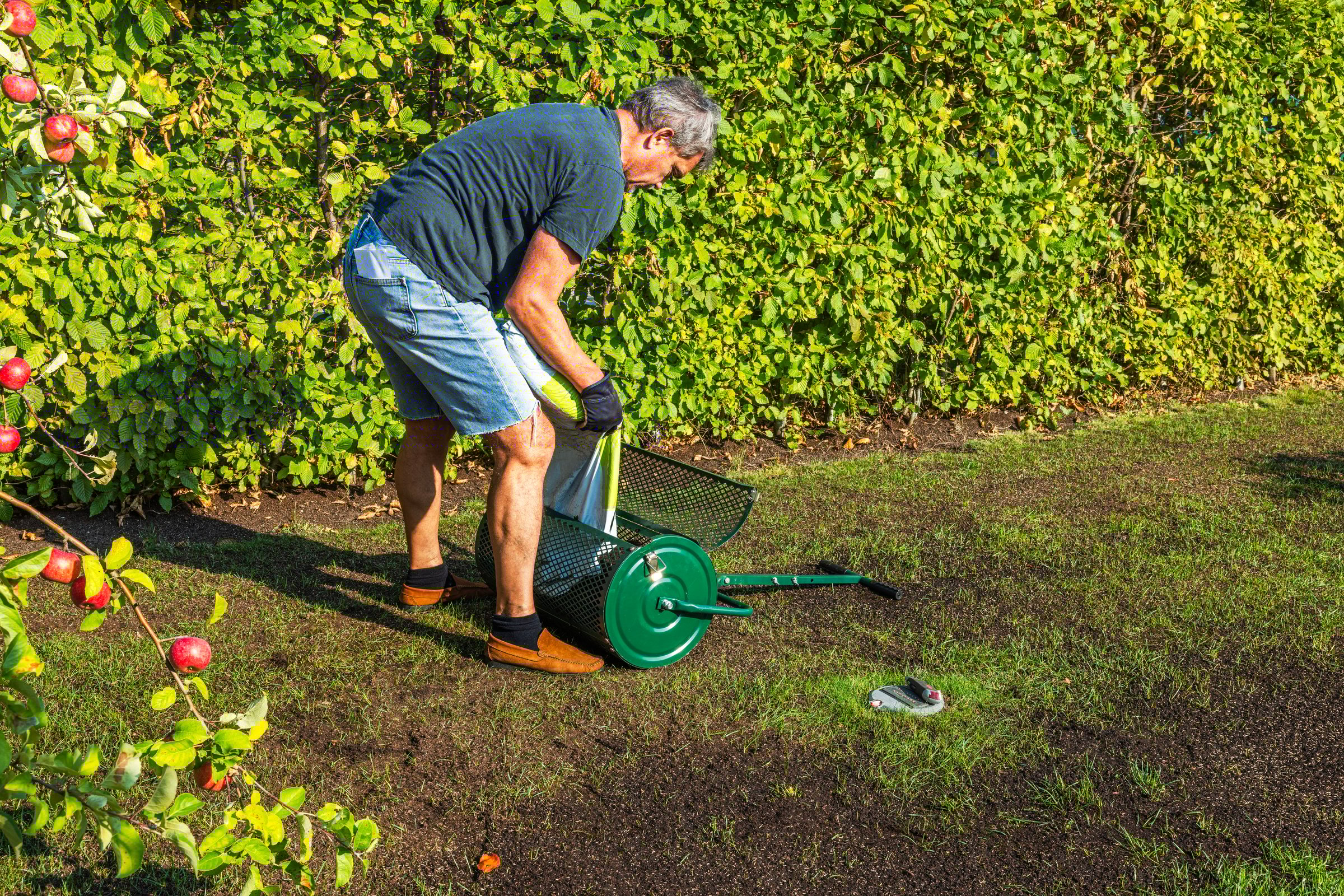 Man is seen loading top dresser with soil from large plastic bag of lawn restoration in residential garden. Sweden.