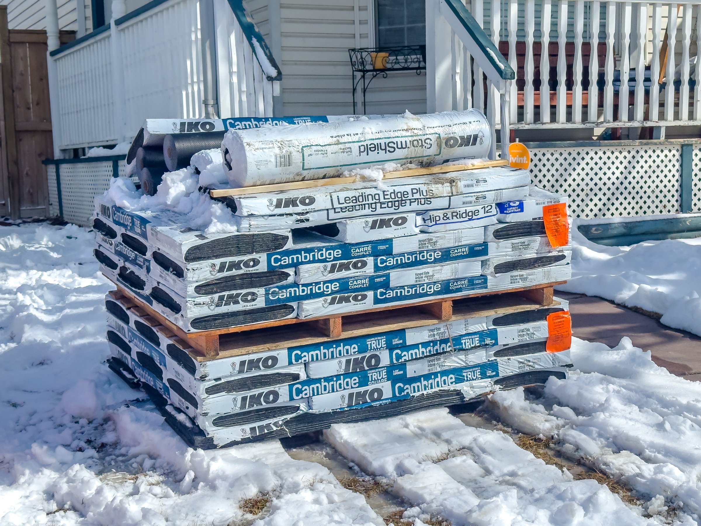Calgary, Alberta, Canada. Apr 4, 2025. A roofing supplies from IKO, including shingles and underlayment, are stacked on pallets in a snowy residential area, likely for a home renovation