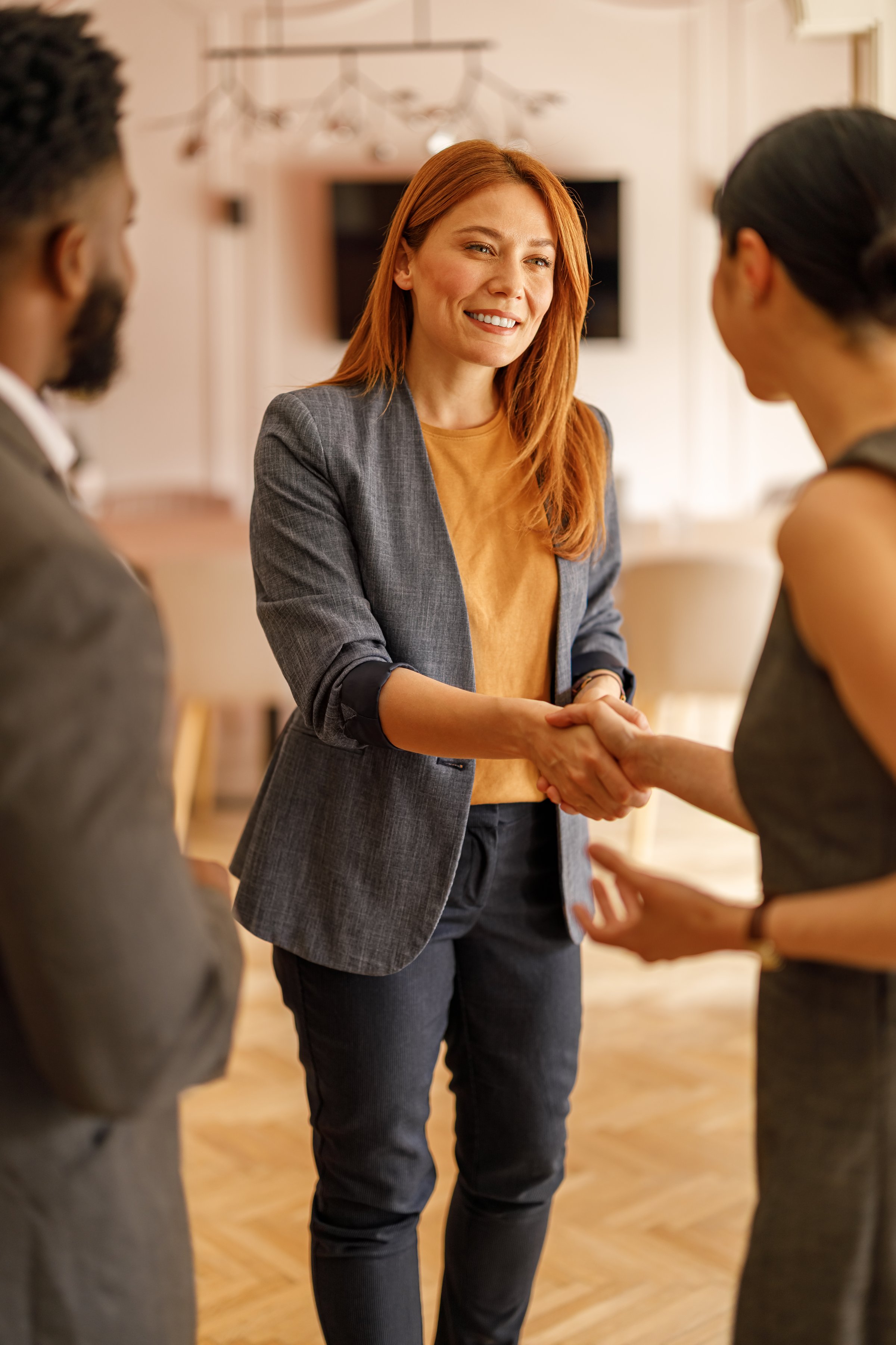 Smiling female executive welcomes colleagues with handshake in corporate office during team meeting