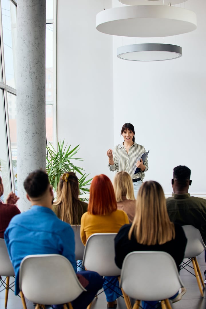 Speaker presenting to an attentive audience in a well-lit modern seminar environment.