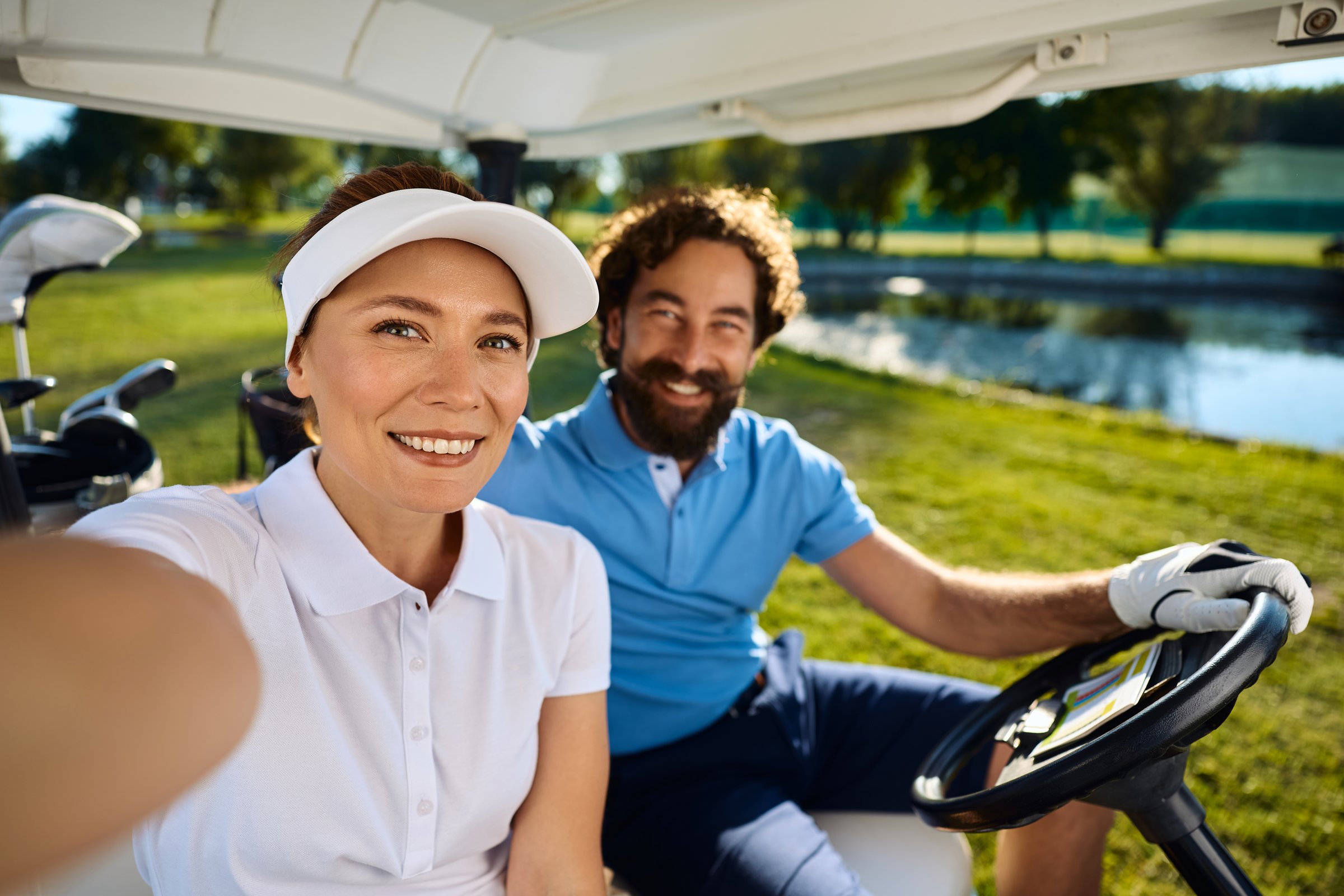 Happy golfers in a buggy taking selfie and looking at camera.