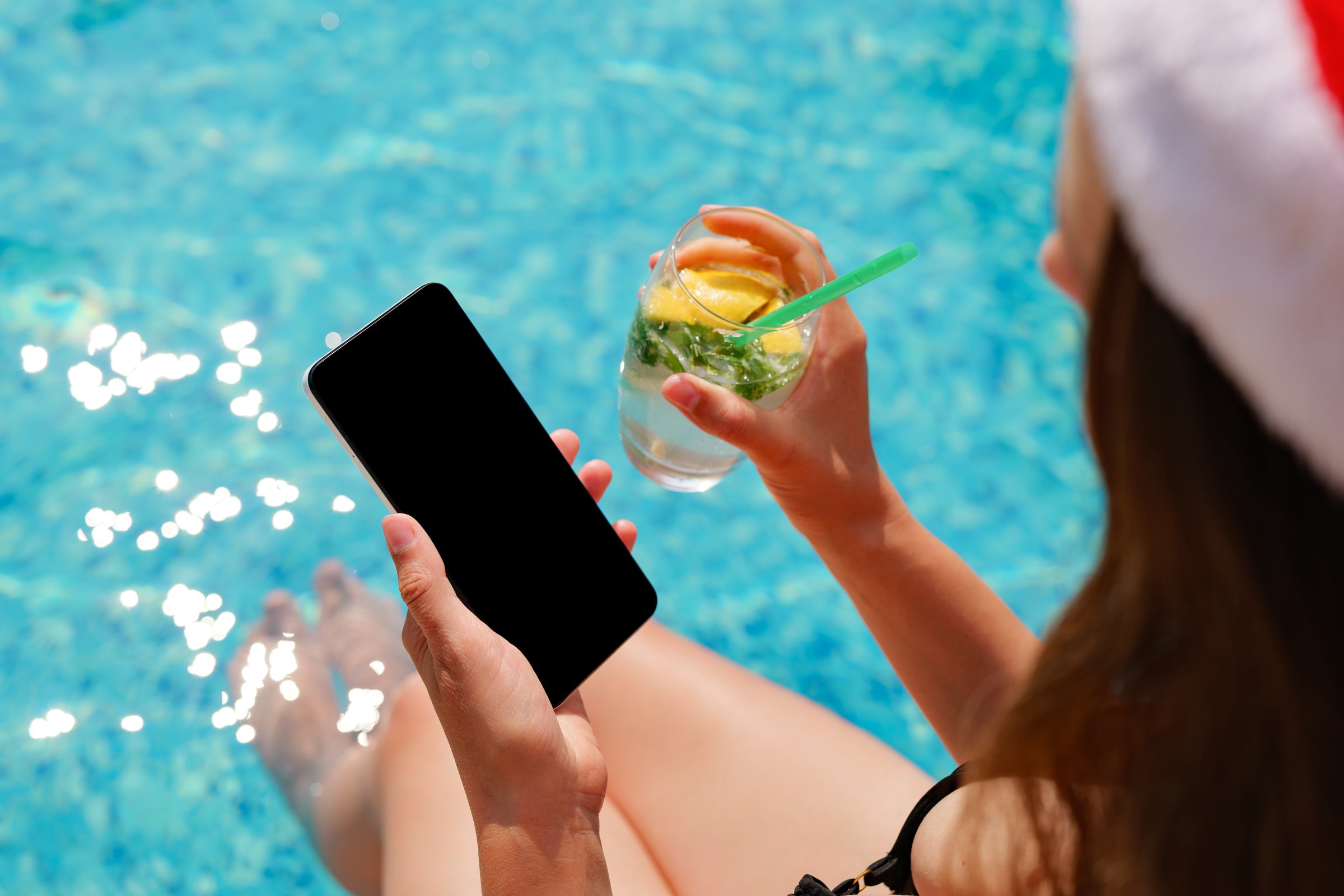 Relaxing by the pool, someone sips a cool beverage and checks their phone on a warm, sunny afternoon.