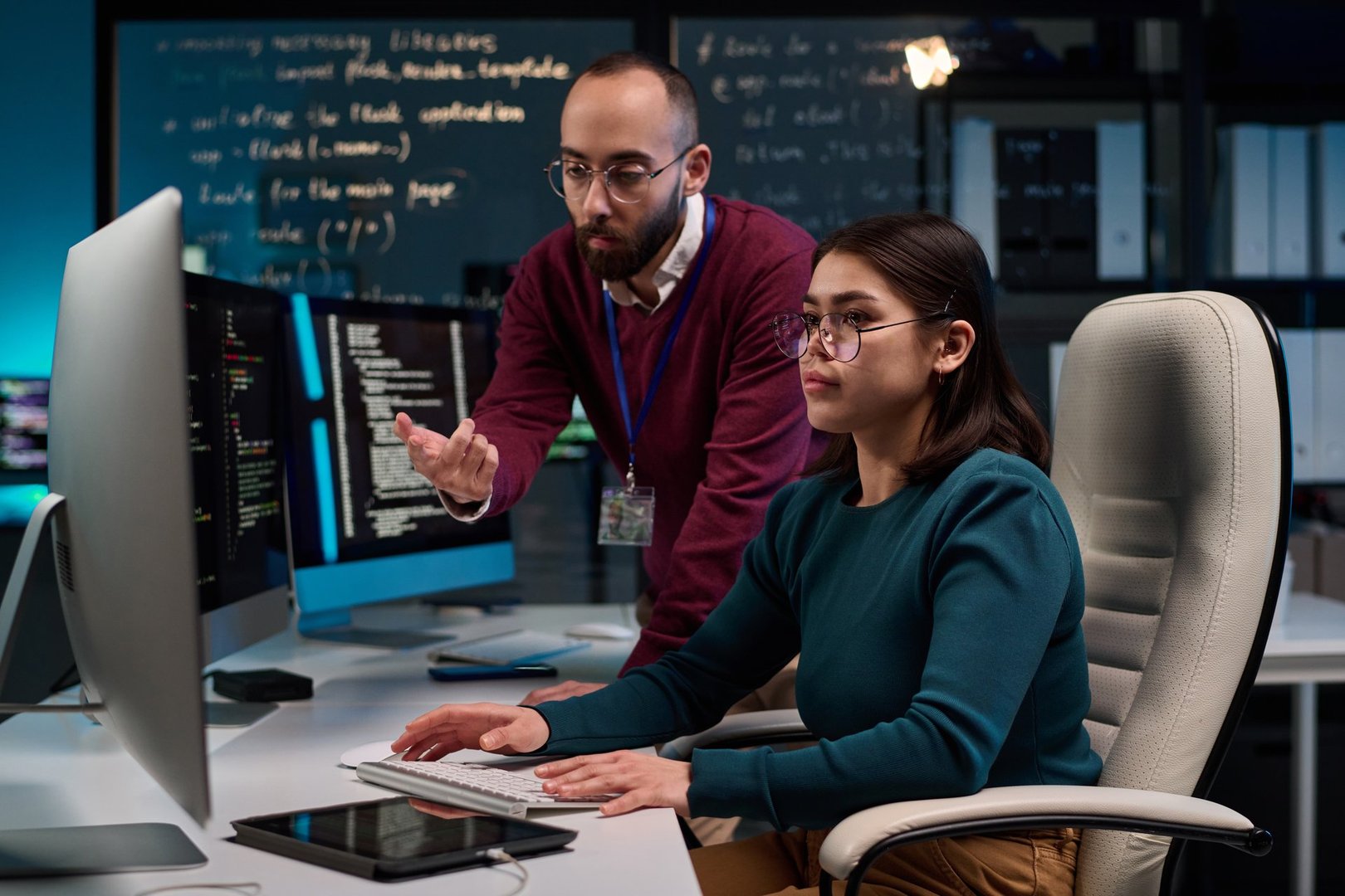 Portrait of young woman using computer in software development office with senior mentor giving advice and pointing at screen copy space