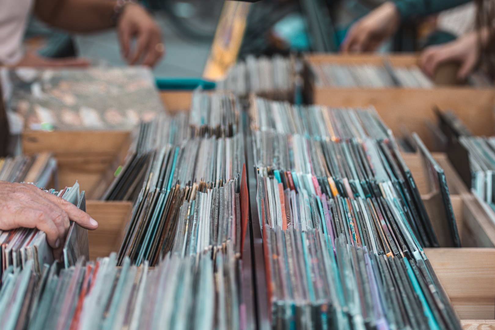 People browsing vinyl records in wooden crates at a music store or flea market. Close-up of hands flipping through vintage LP albums, symbolizing retro music culture, nostalgia, and collecting