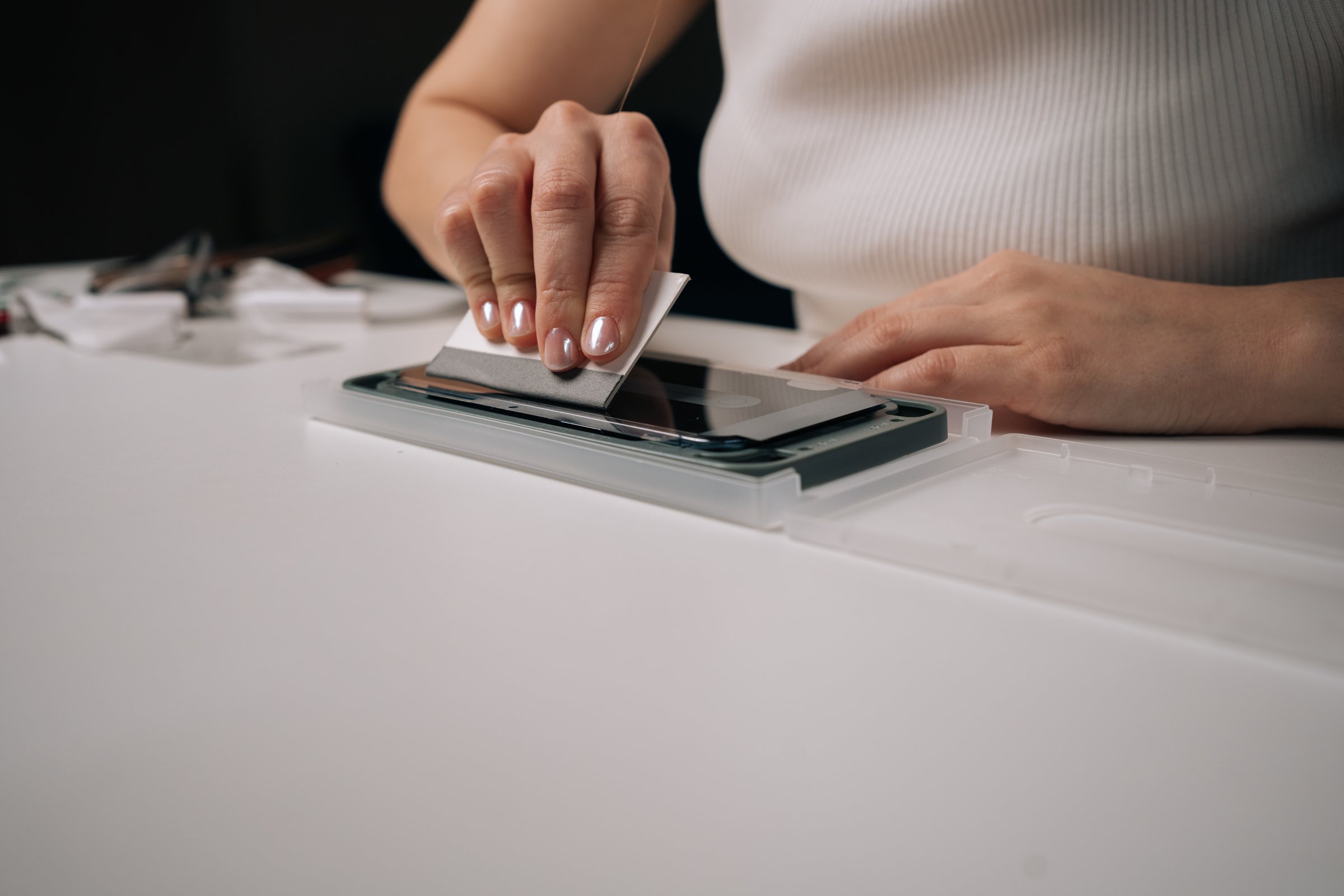 Skilled technician carefully applying smartphone screen protector with specialized machine, using squeegee for precise, bubble-free installation. Concept of mobile phone maintenance and service.