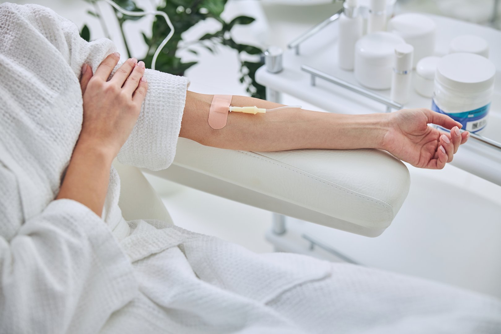 Cropped head portrait of unrecognized female patient sitting in medicine armchair while receiving IV infusion in wellness center