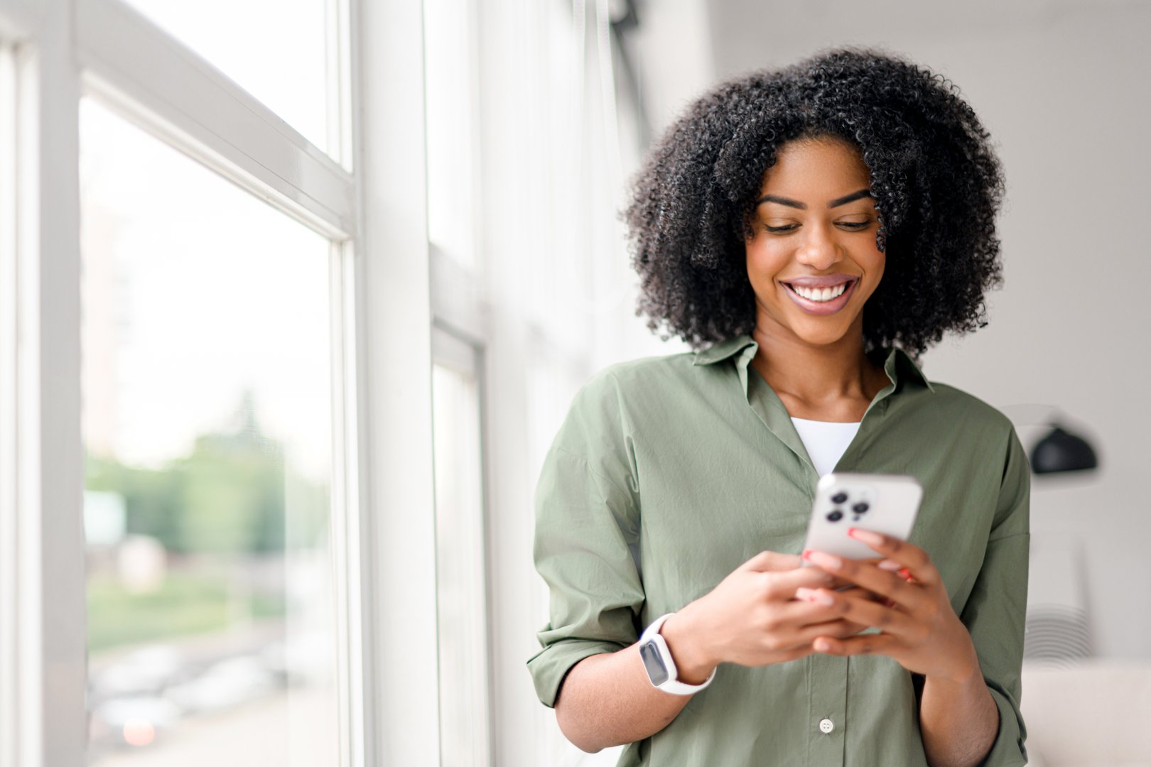 In a well-lit indoor setting, an African-American woman with a contagious smile interacts with her smartphone, engaging with friends or followers through a social network.
