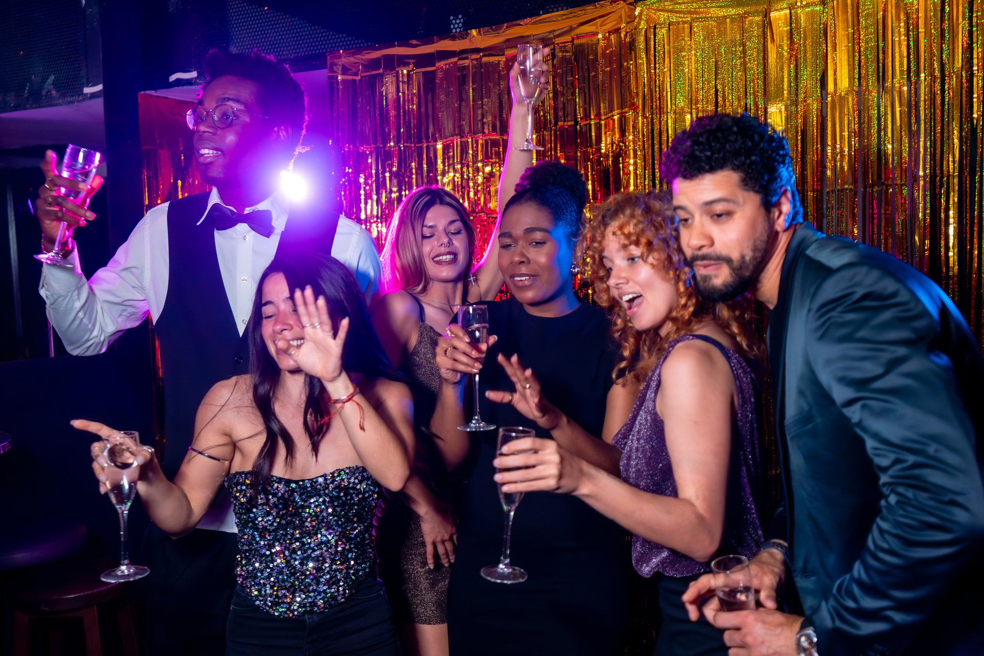 Group of cheerful, multi-ethnic friends enjoying champagne and dancing together, celebrating life in a vibrant nightclub atmosphere