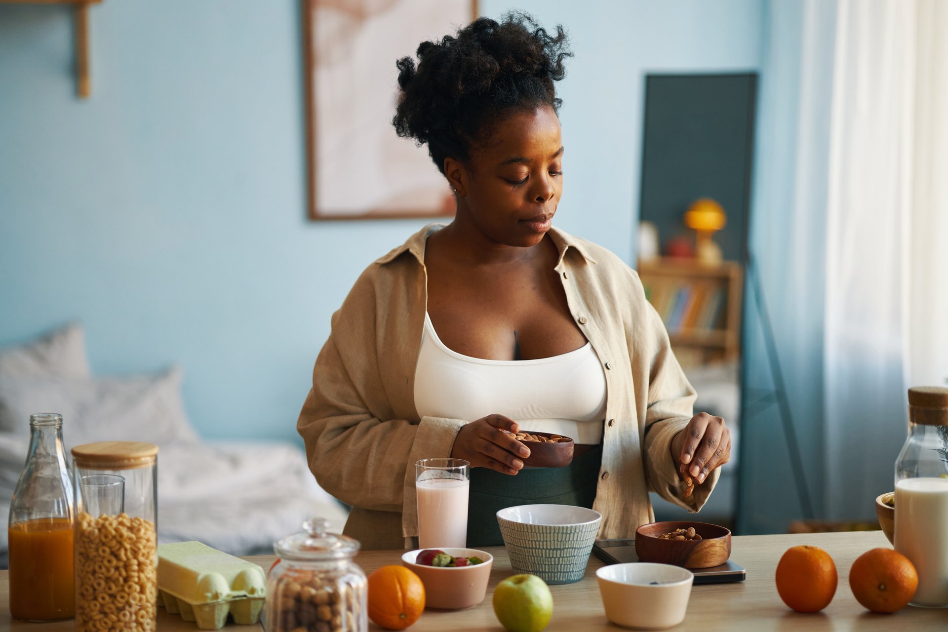 African American woman preparing breakfast with fresh fruits, cereal, and a smoothie in a neatly arranged kitchen