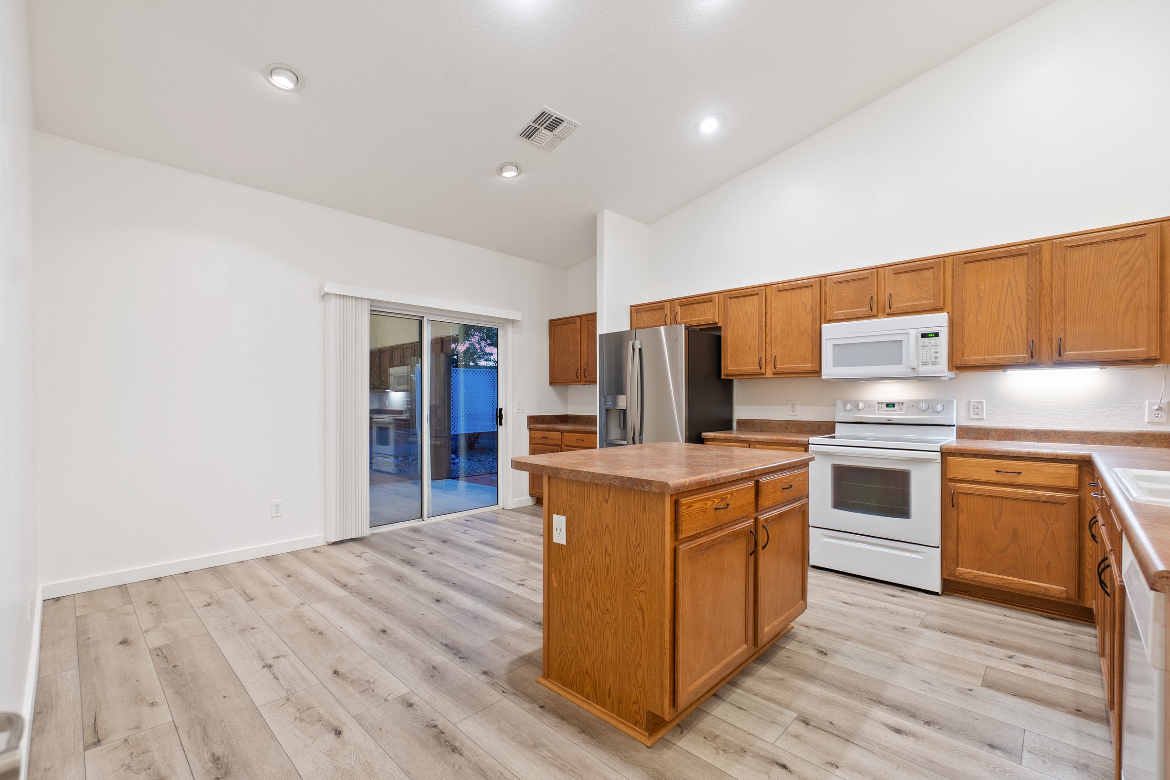 The spacious kitchen is completely empty, featuring beautiful wooden cabinets and a large central island that enhances its charm