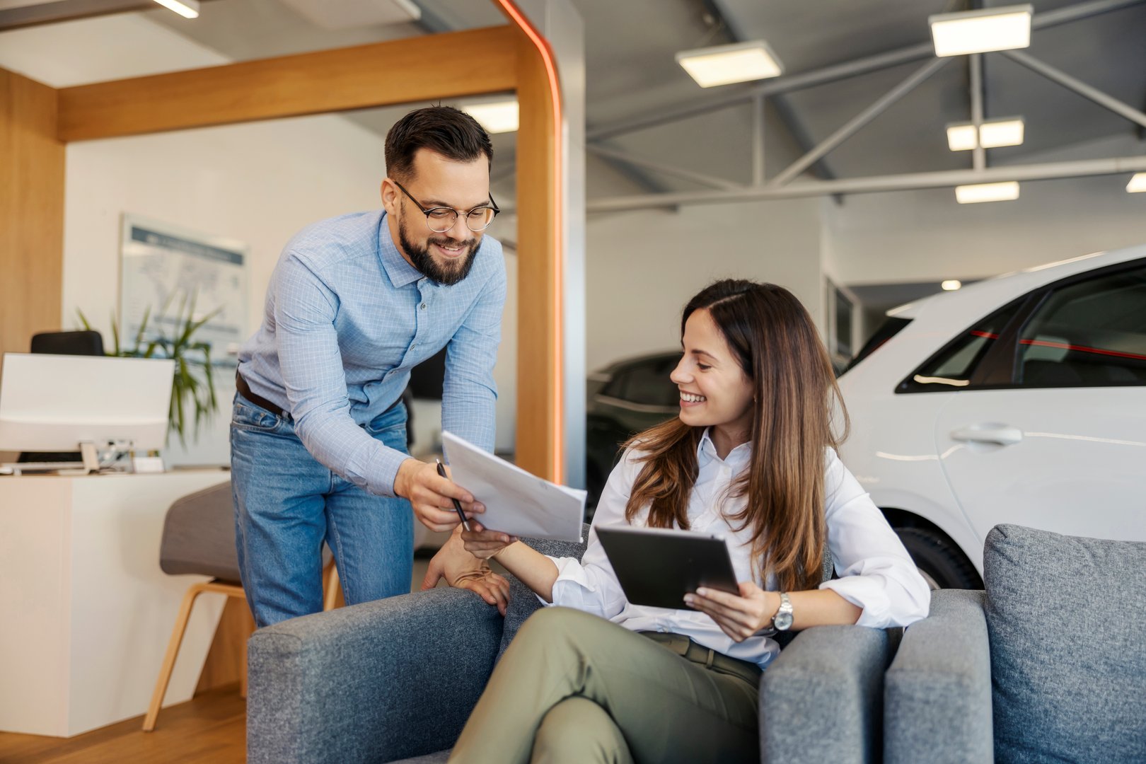Car dealer giving paperwork and contract to a female customer at car salon.