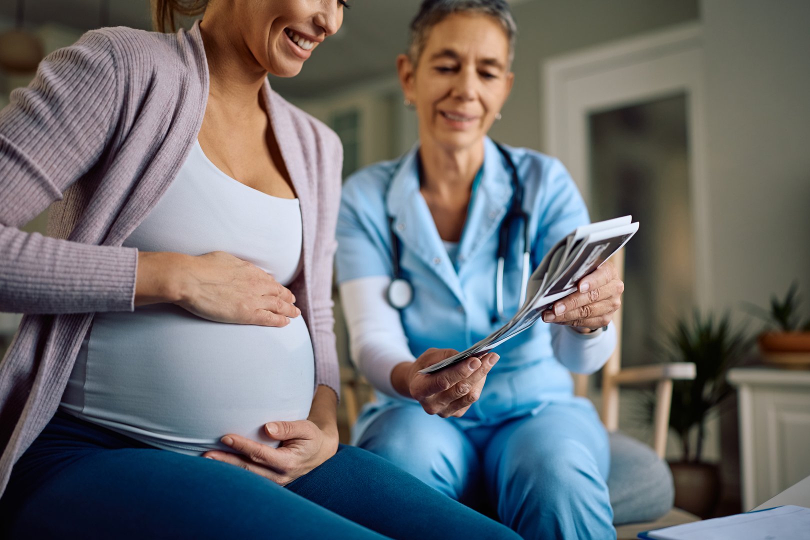 Happy expecting mother looking at medical scan of her baby with a nurse during home visit.