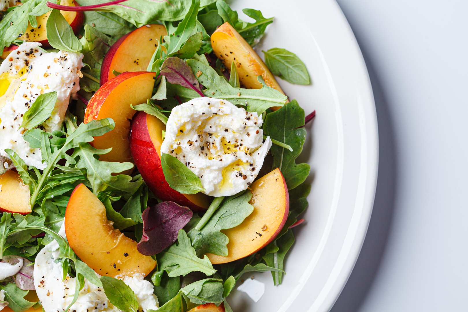 Burrata and peaches summer salad, white background, top view. Italian recipe concept.