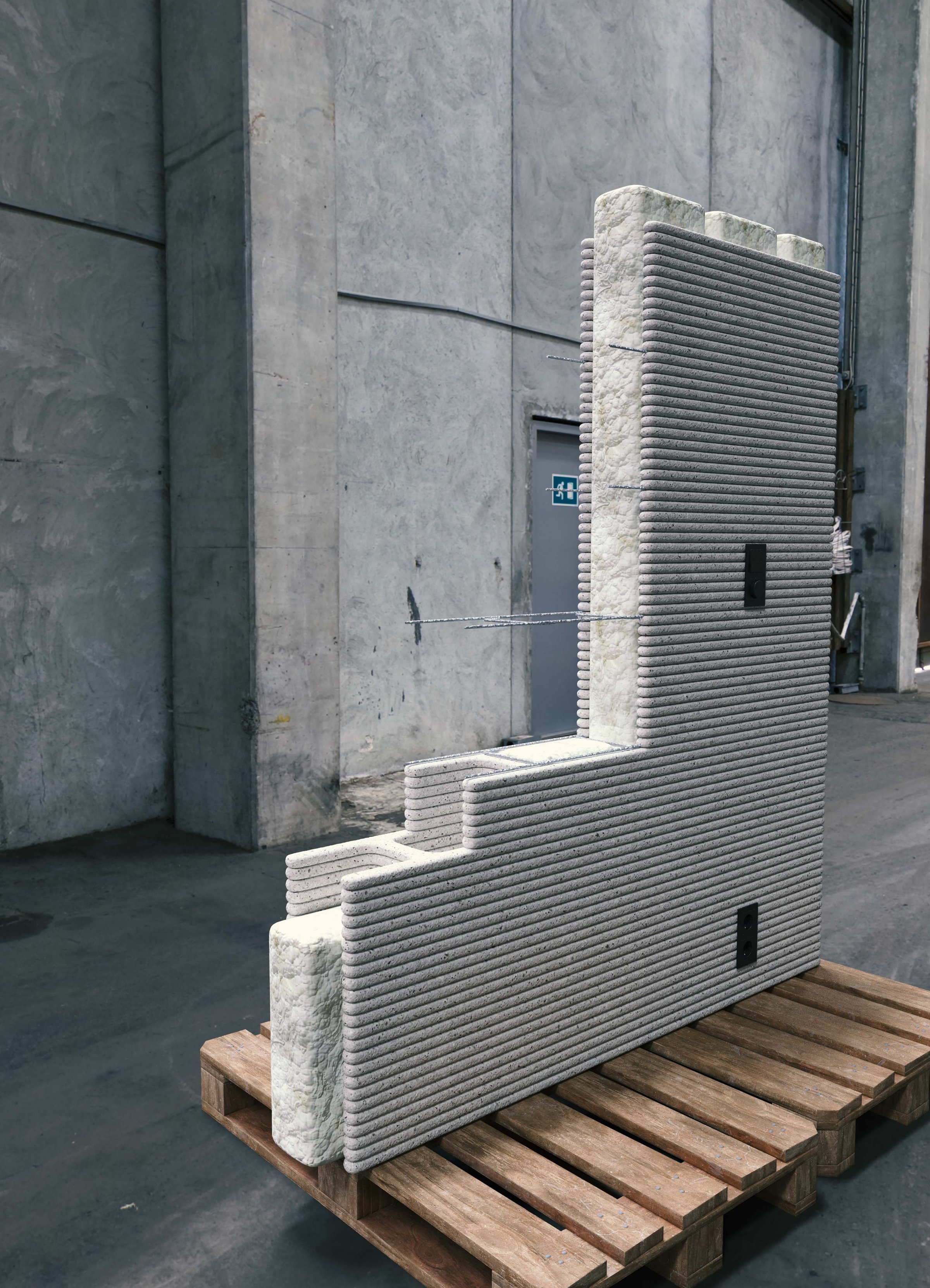 A 3D-printed concrete wall section with a textured surface on a wooden pallet in an industrial setting.