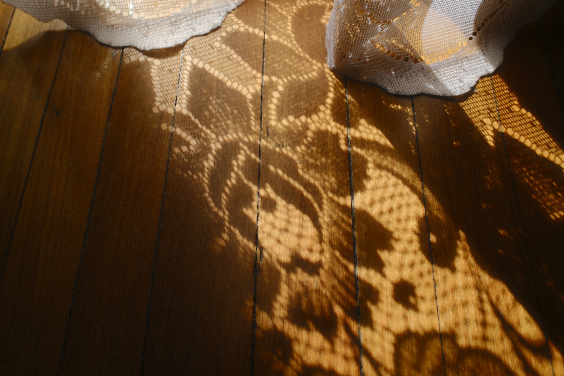 Sunlight filters through lace, creating shadows on an old wooden floor.