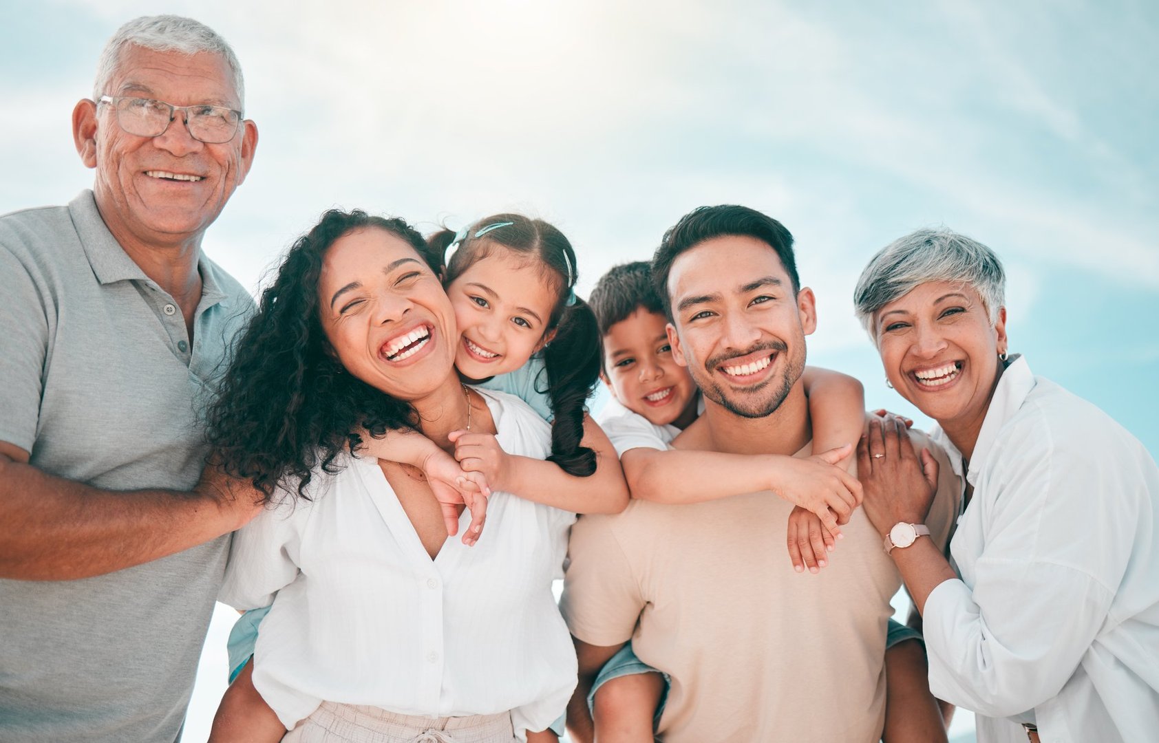 Family portrait outdoors with grandparents, parents, and kids smiling together on holiday.