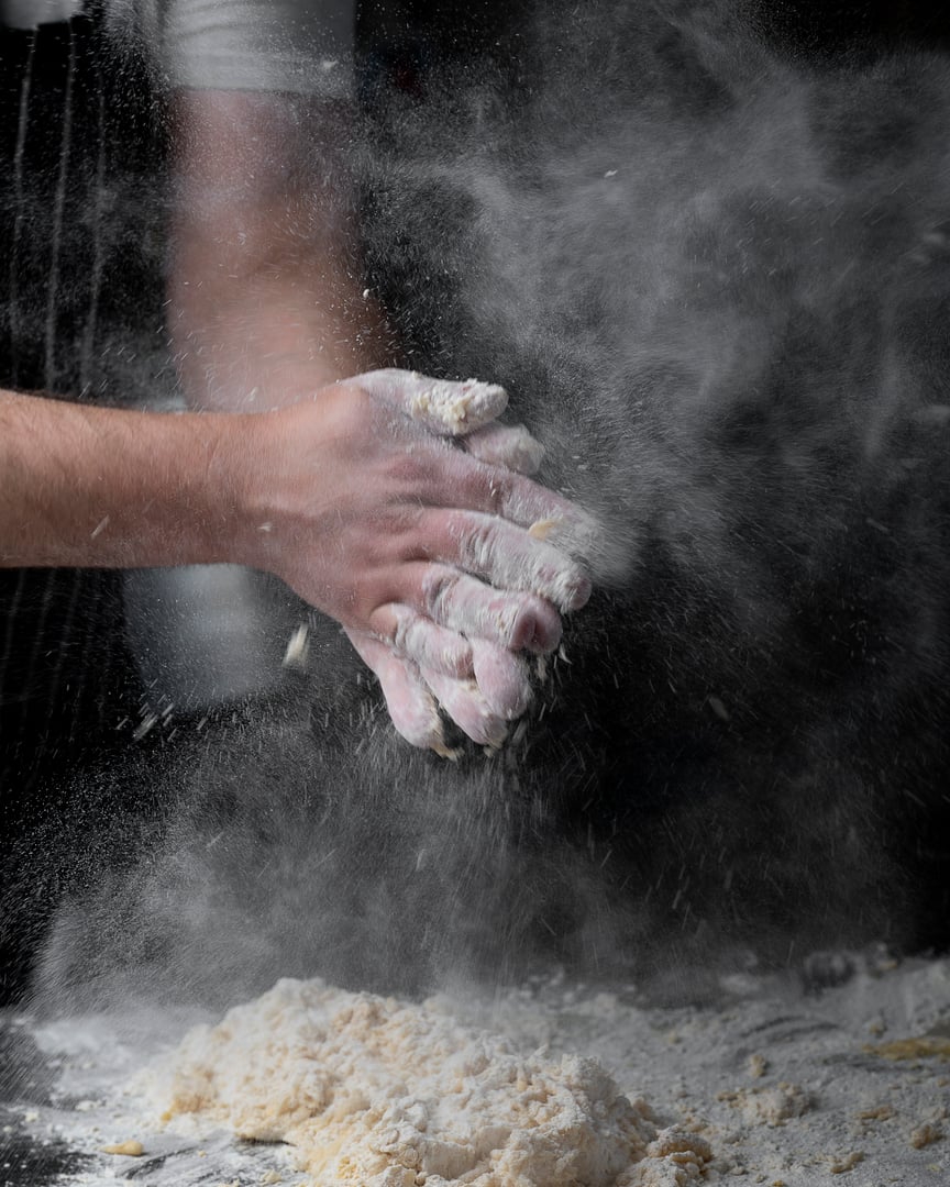 Beautiful and strong men's hands knead the dough make bread, pasta or pizza. Powdery flour flying into air. chef hands with flour in a freeze motion of a cloud of flour midair.