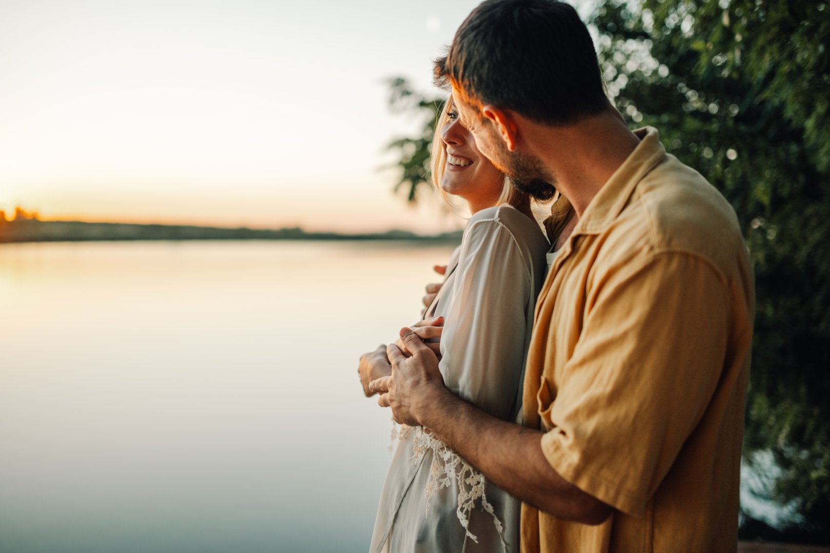 Happy couple embracing and enjoying a romantic moment by the tranquil lake at sunset, radiating love and creating a serene atmosphere filled with joy and intimacy
