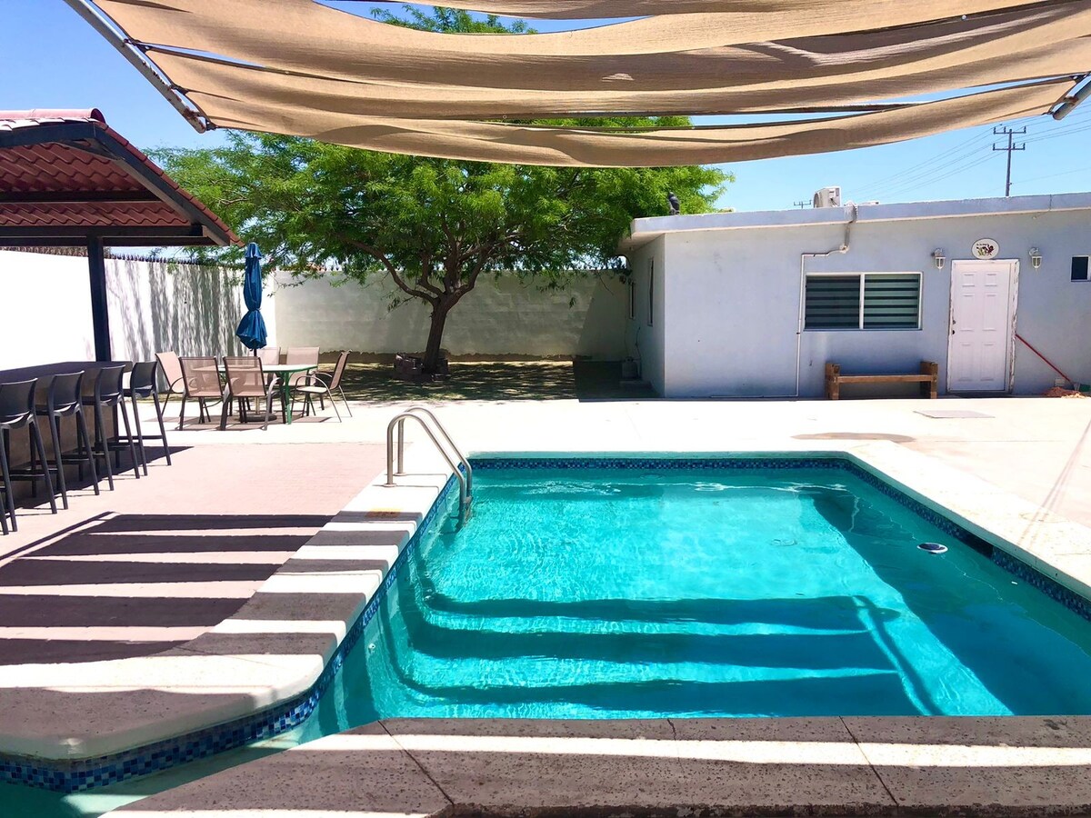 A luxurious backyard with a swimming pool, hot tub, and patio furniture at a modern house during sunset.