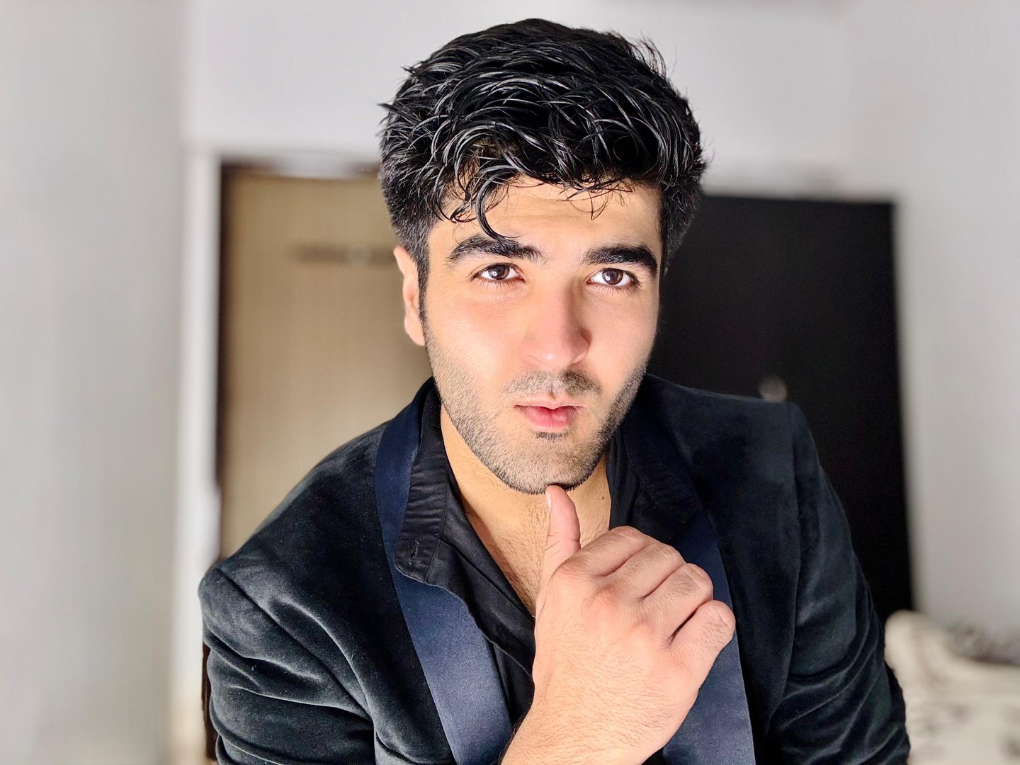 Man in a dark suit posing indoors, with one hand on his chin and expression of confidence.