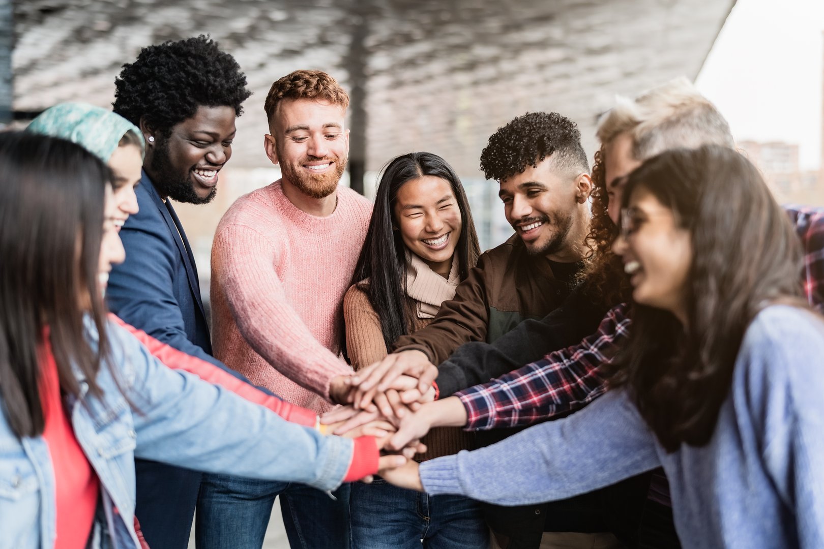 Young multiracial friends stacking hands together outdoor - Friendship and diversity concept