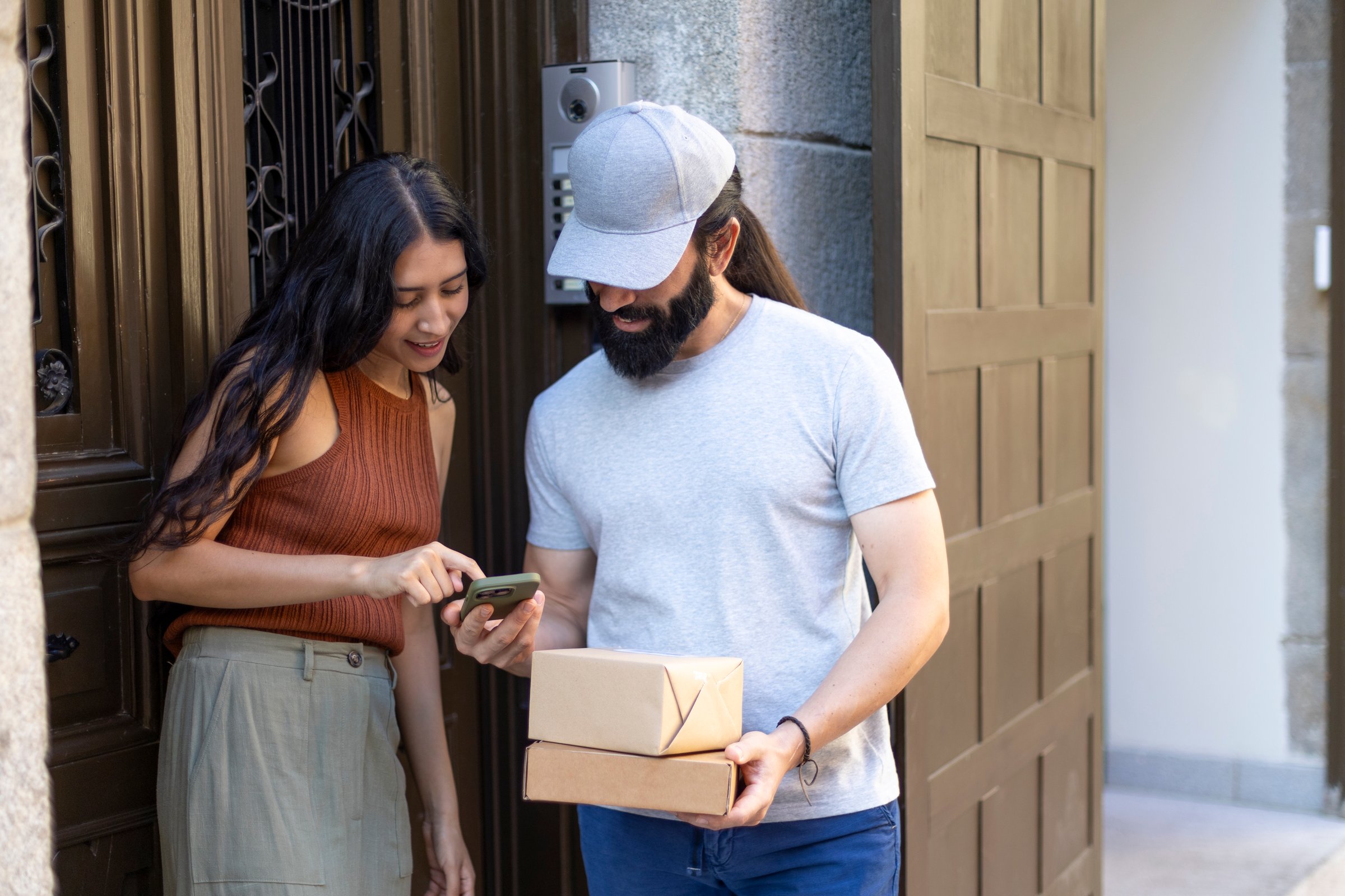 Delivery man holding a package and showing a smartphone to a woman while standing at the entrance of a building