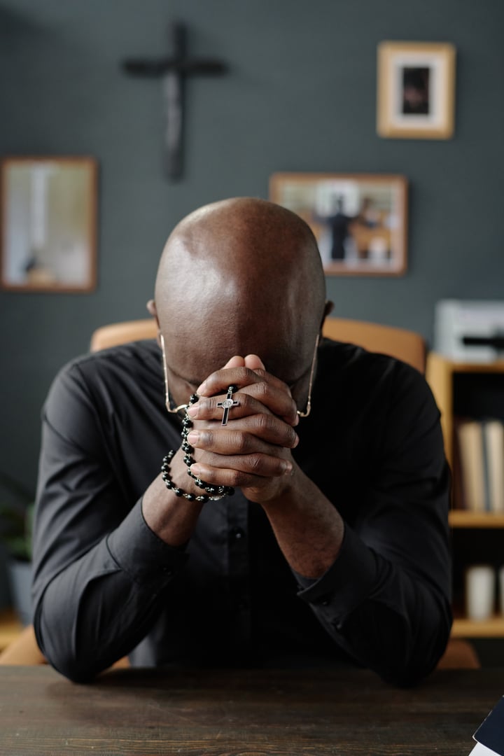 Vertical shot of African American pastor praying silently alone in office