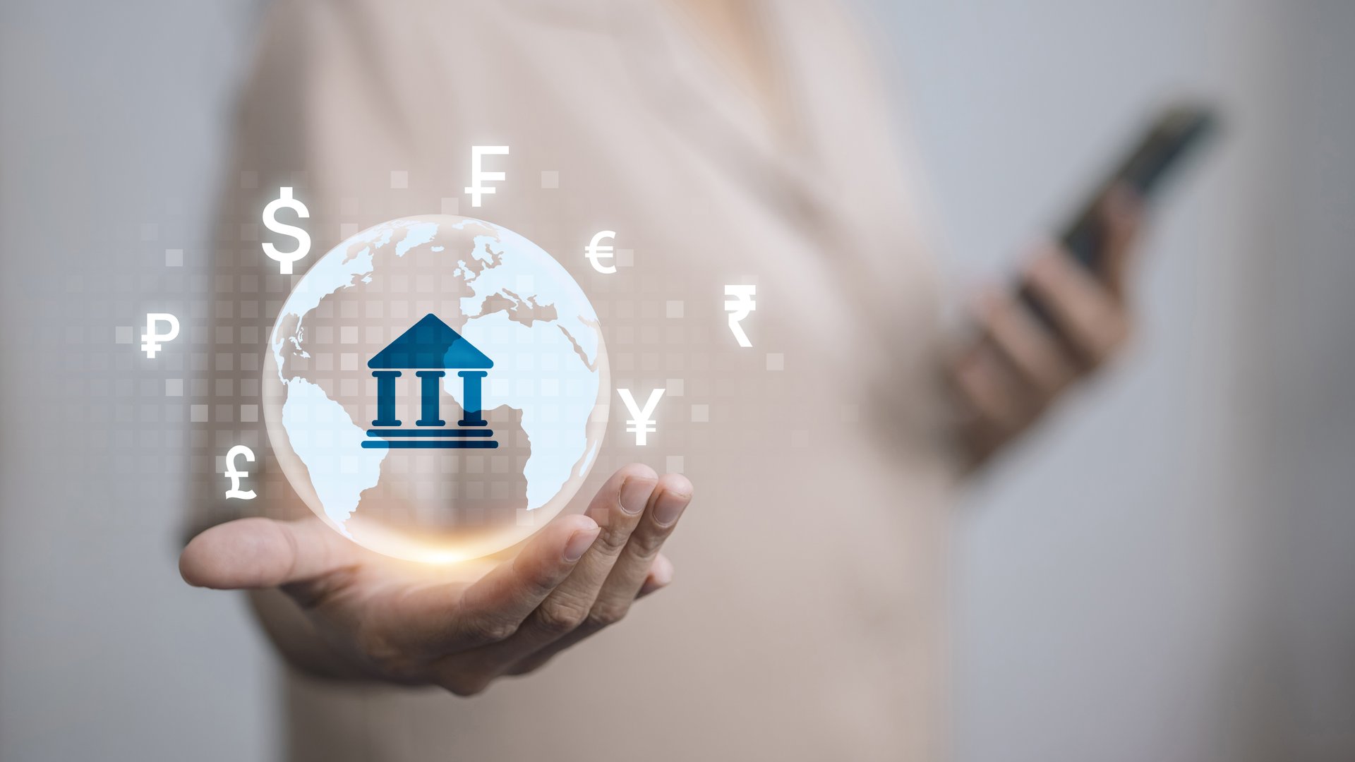Hand holding holographic globe with bank icon and currency symbols, representing global banking, digital finance, and foreign exchange.