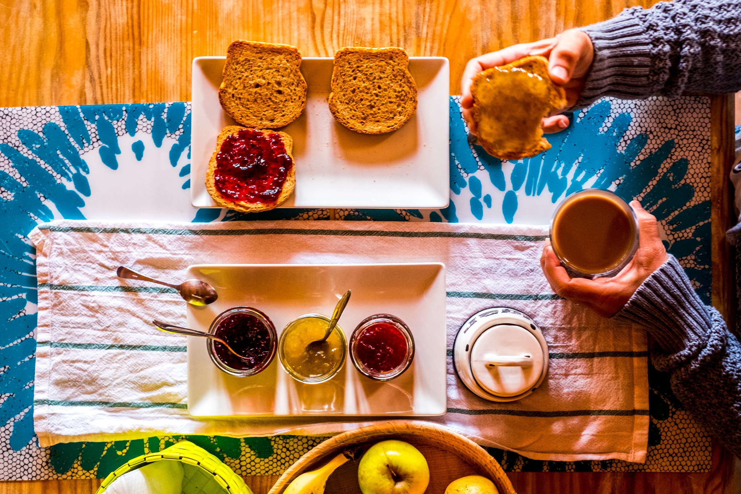 Breakfasy healthy morning time viewed from vertical above view  people woman with toasted bread and marmalades on a wooden tble drinking cappuccino coffee - focus on marmalades