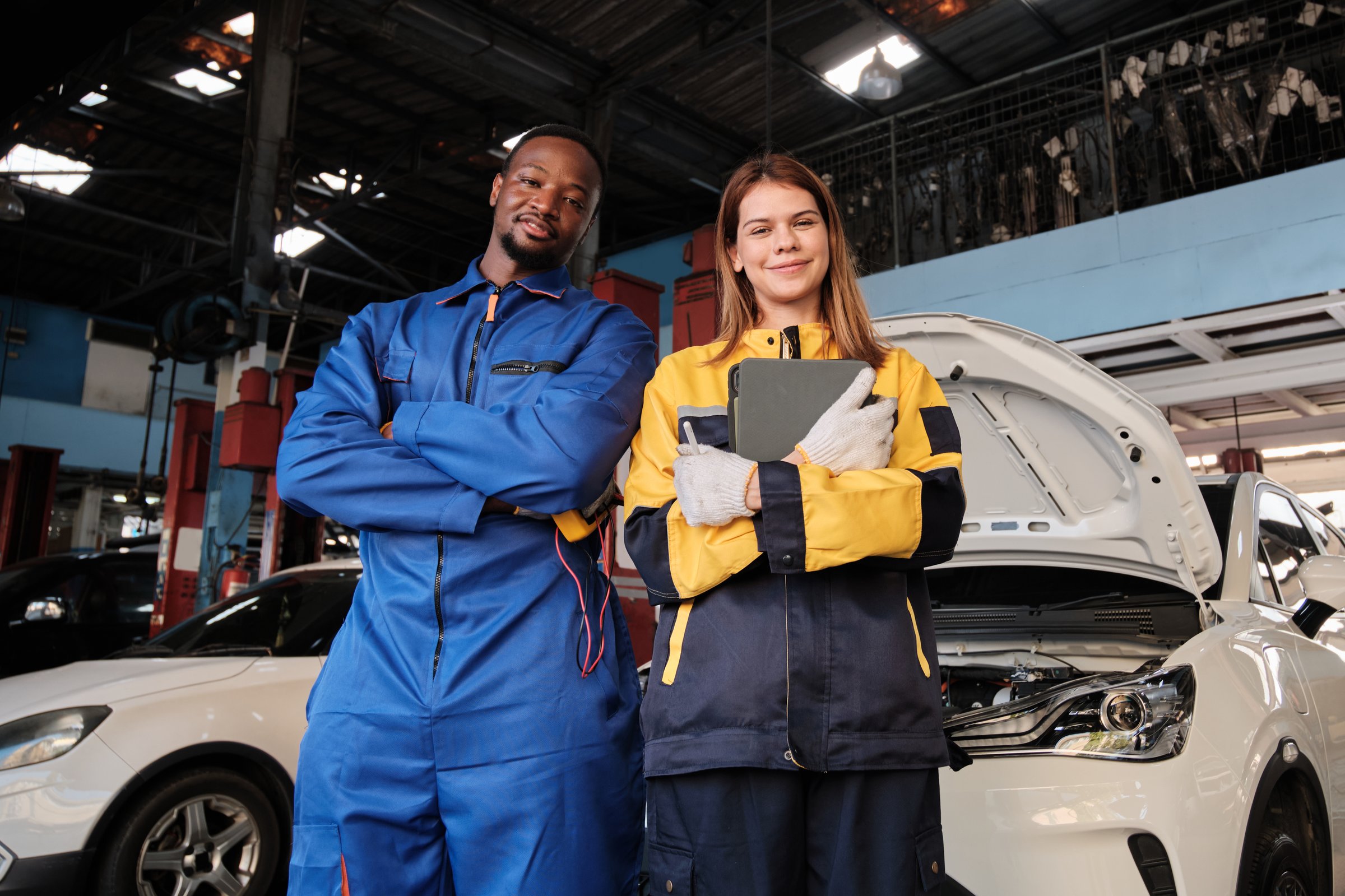 Happy professional teamwork, White female inspector engineer and Black mechanic man cheerful, arms crossed with smile in fix car garage, maintenance service jobs in automotive transportation industry.