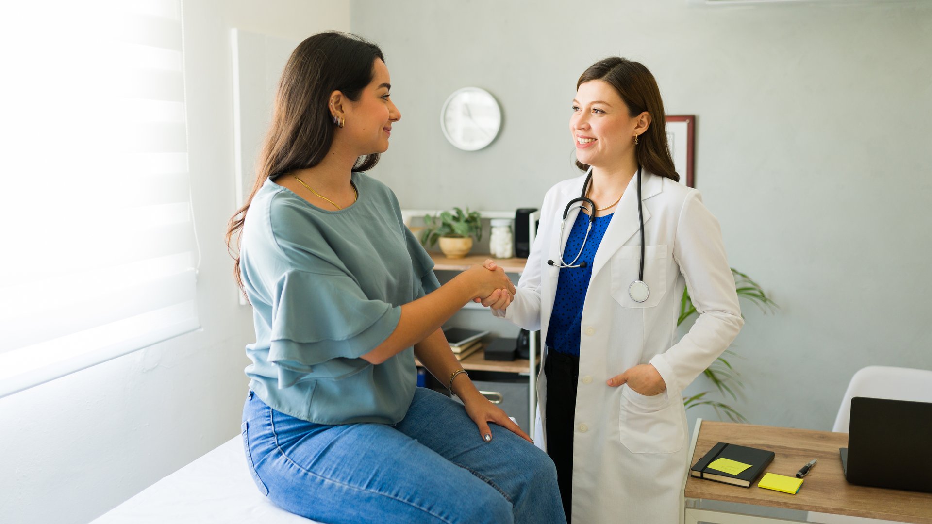 Female doctor happily shaking hands with her hispanic patient after a successful consultation in her office