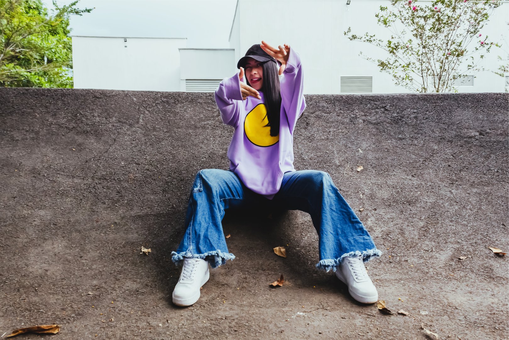 beautiful teen girl in sweatshirt and cap sitting in the city in urban style posing to the camera, happy trendy latin girl outdoors