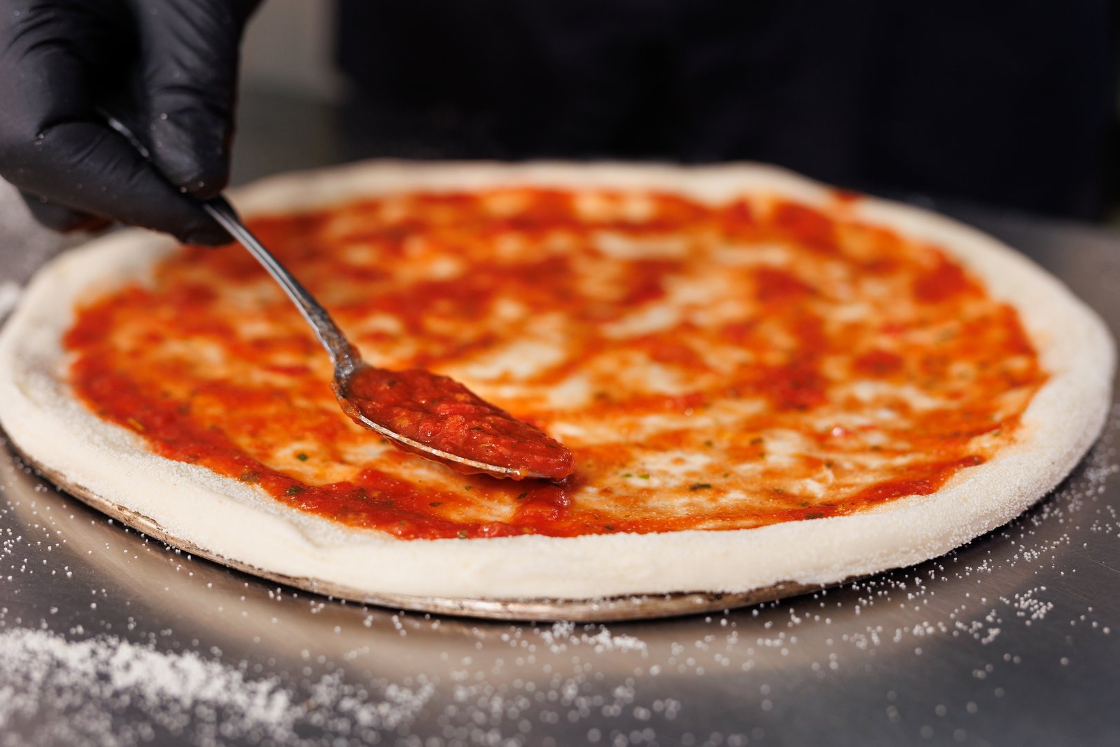 The chef spreads tomato sauce on a pizza pan