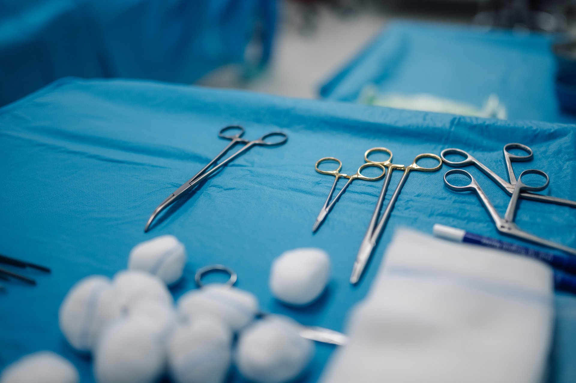 A close-up shot of various surgical instruments including scissors and forceps arranged neatly on a blue, sterile cloth, ready for an upcoming medical procedure.