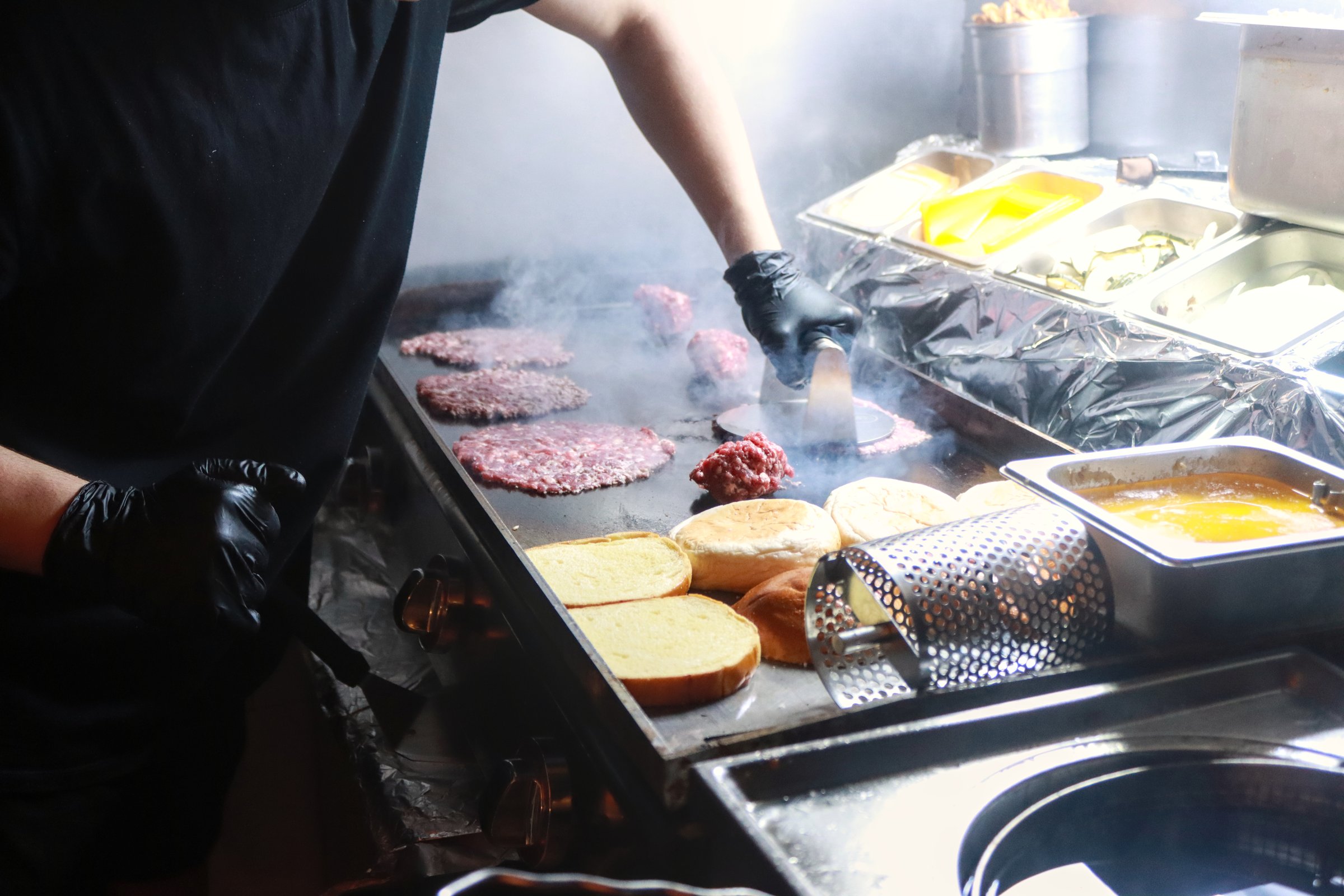 Chef preparing smash burgers on a hot griddle, pressing meat patties and toasting buns, capturing the fast-paced cooking process in a busy commercial kitchen.