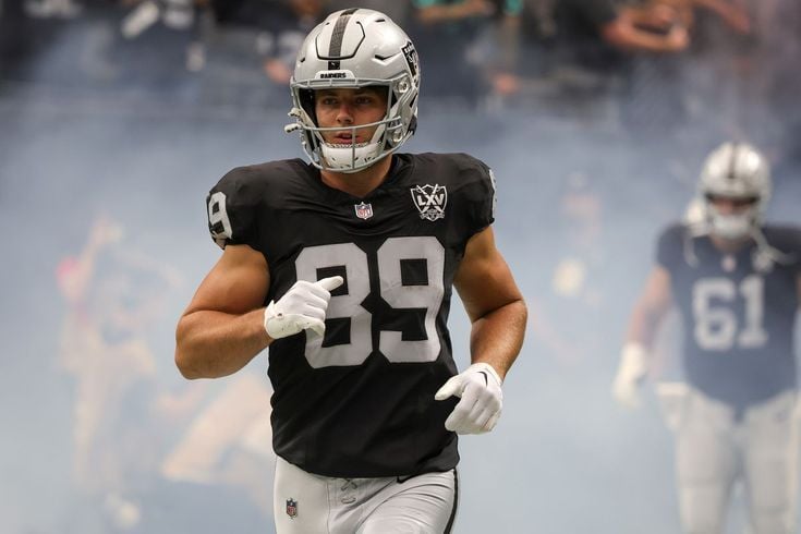 Football player in a black uniform with number 39 runs onto the field through smoke, with a teammate in the background.