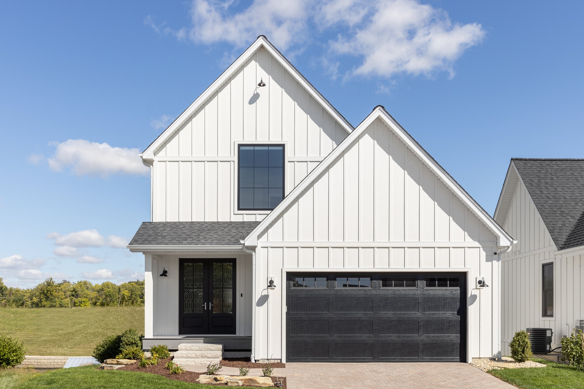 Elmhurst, IL, USA - September 26, 2022: A large, white modern farmhouse with vertical siding, a black two car garage, and lights mounted on the siding.