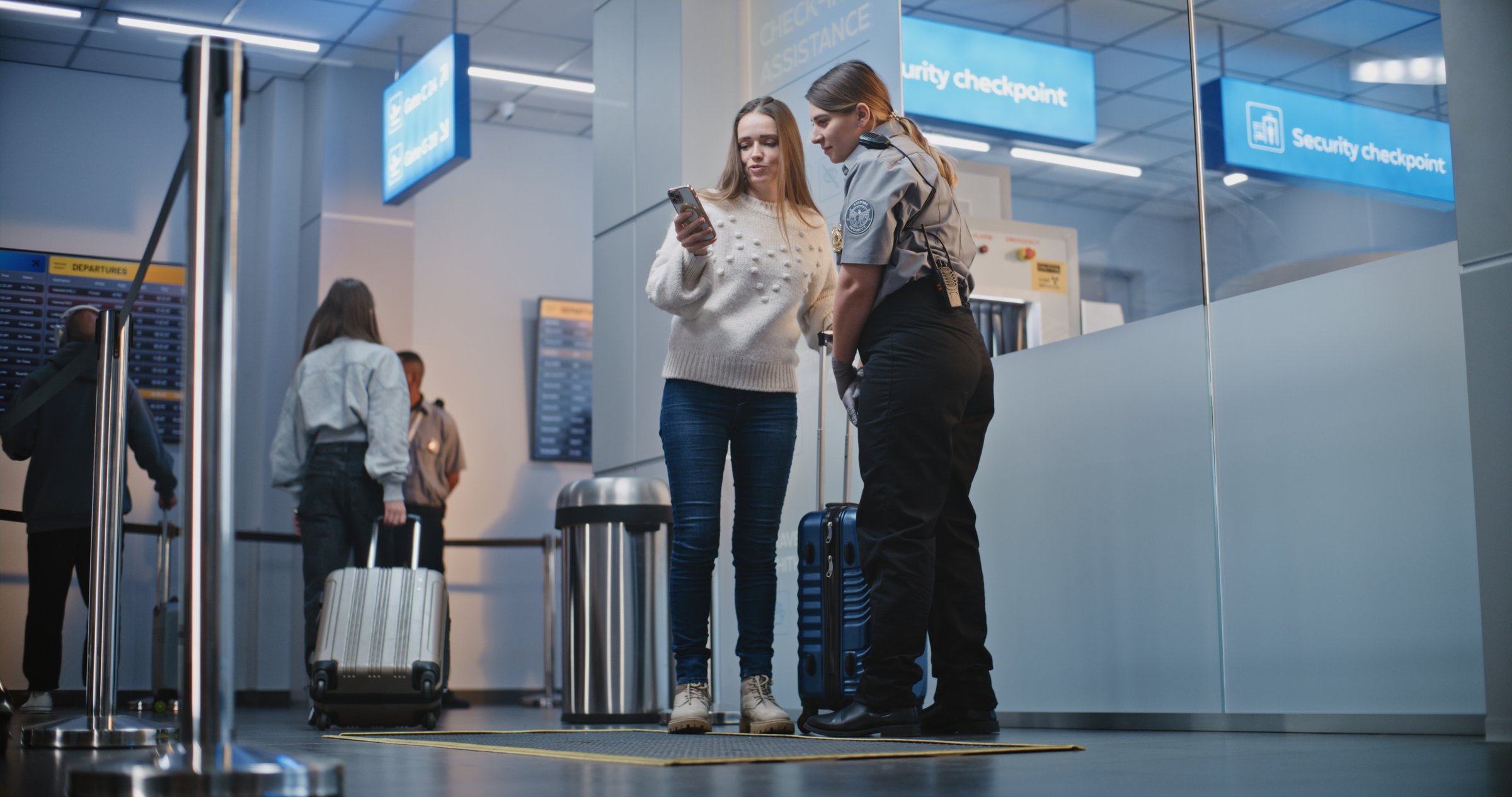 Diverse People, Passengers with Luggage Walking in Crowded International Airport Terminal. Female Security Officer Helps Woman to Find Gate for Boarding Plane Flight. Travelers Going on Vacation Trips