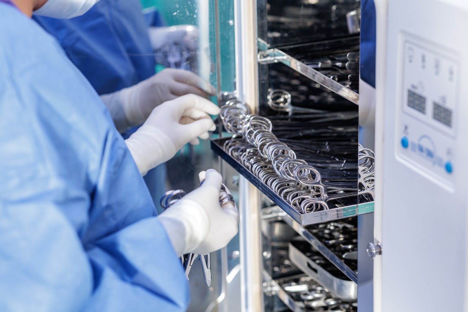 Gloved healthcare worker loads stainless instruments into an autoclave cabinet for aseptic reprocessing and infection control.